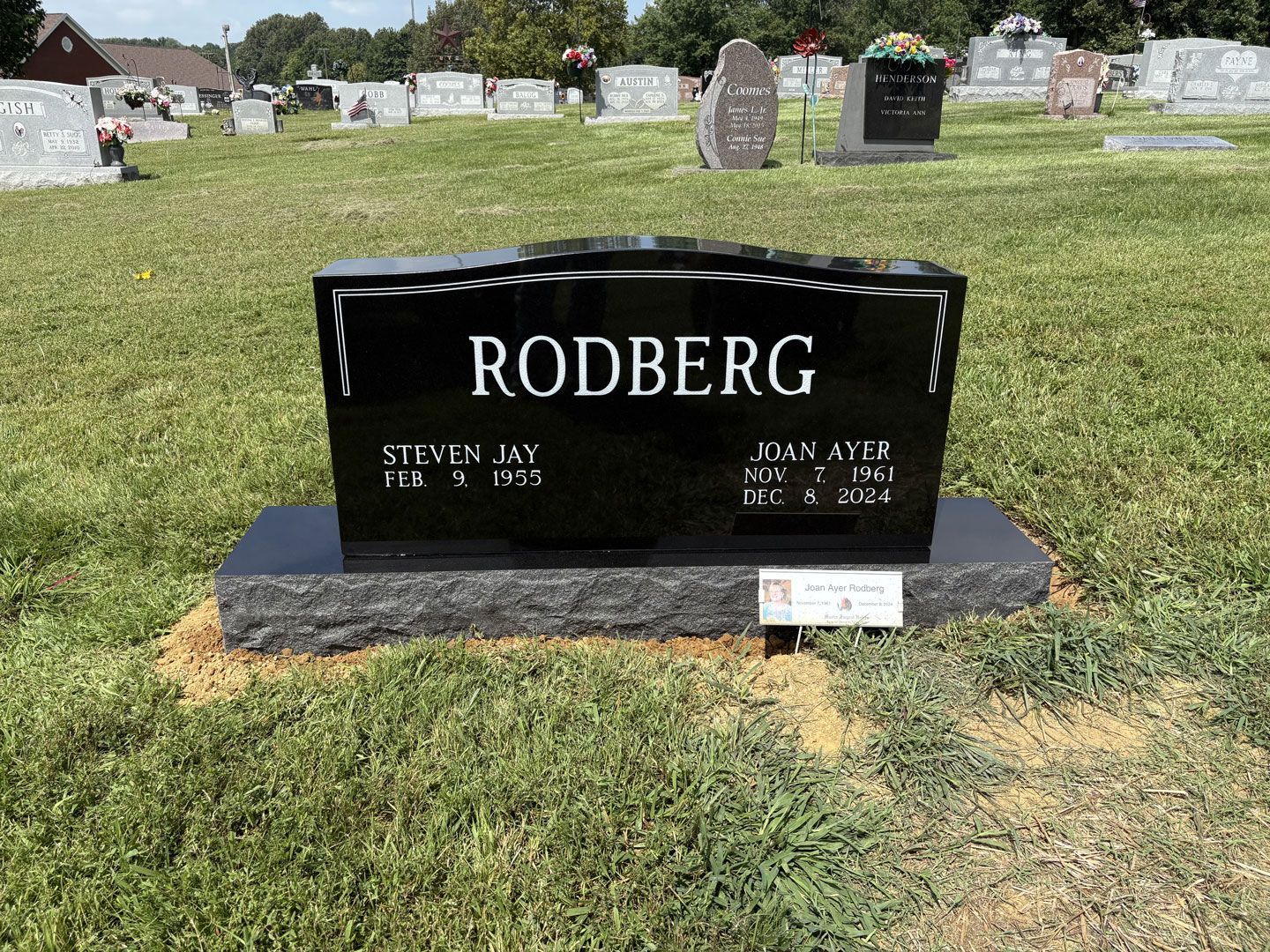 Black headstone in a cemetery. It reads 