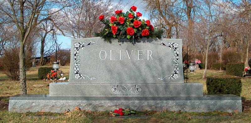 A gravestone for oliver in a cemetery with red roses on top.