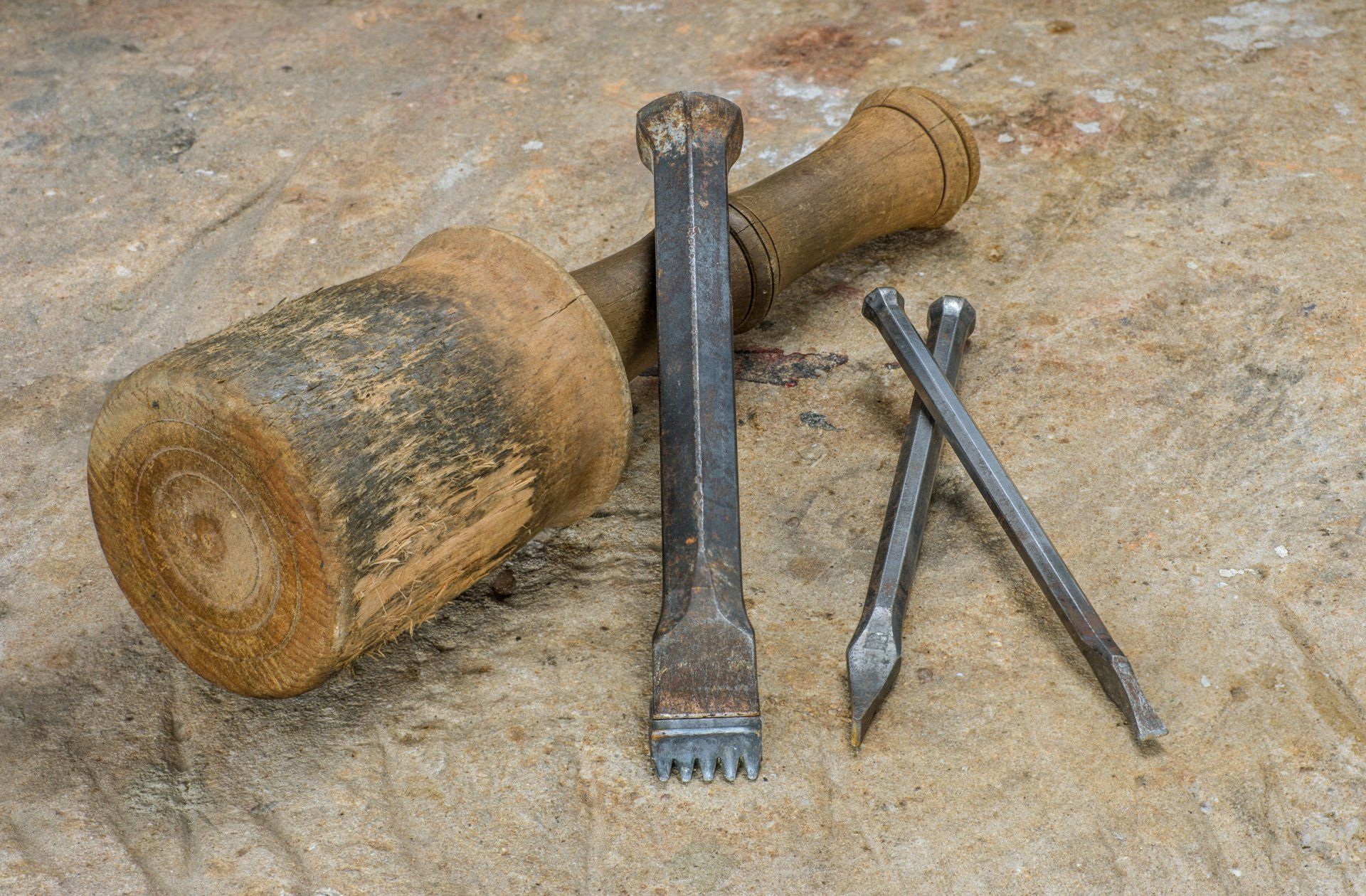 A wooden mallet , chisel , and nails are on a table.