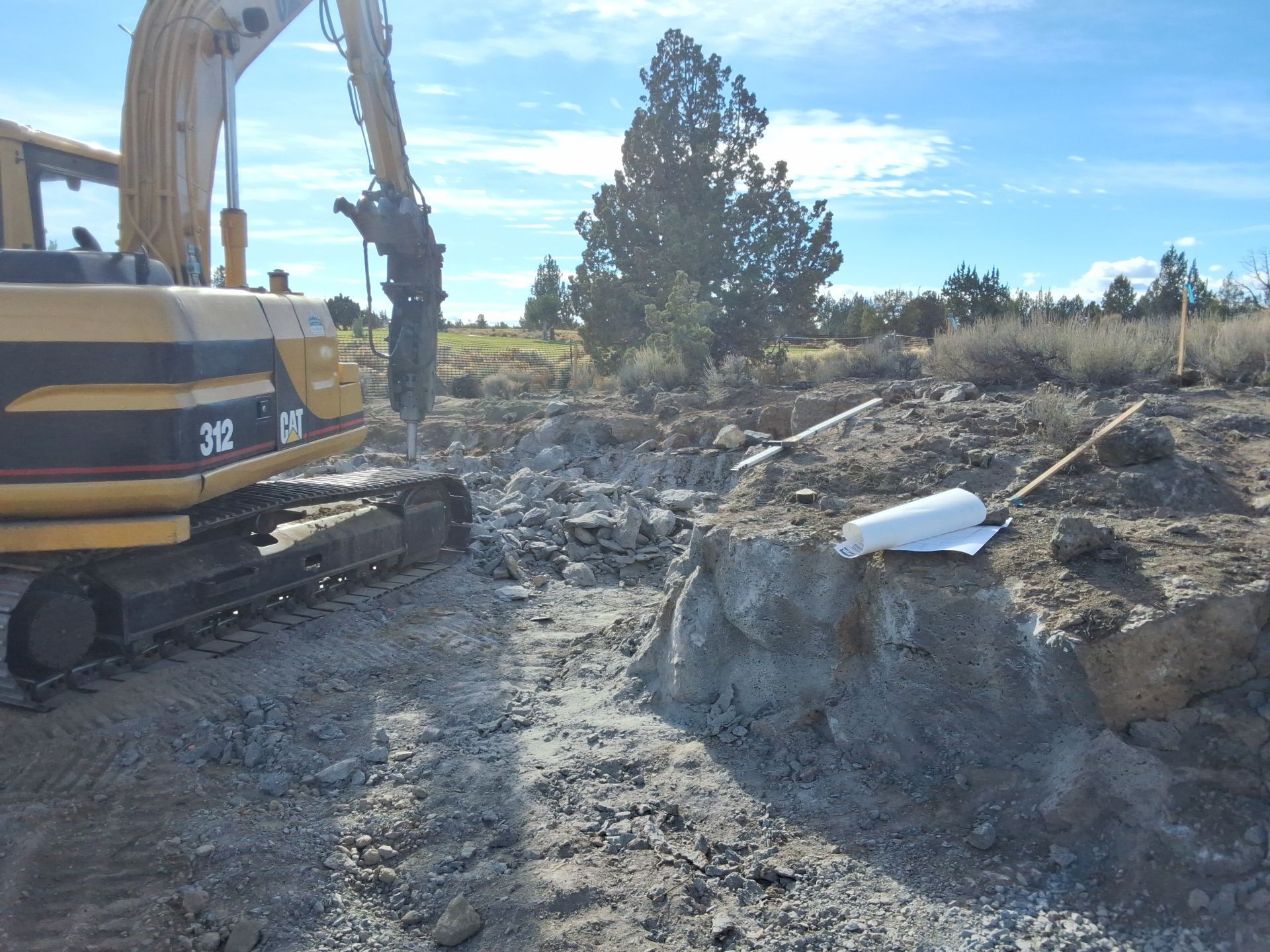 Yellow excavator breaking up concrete outdoors.