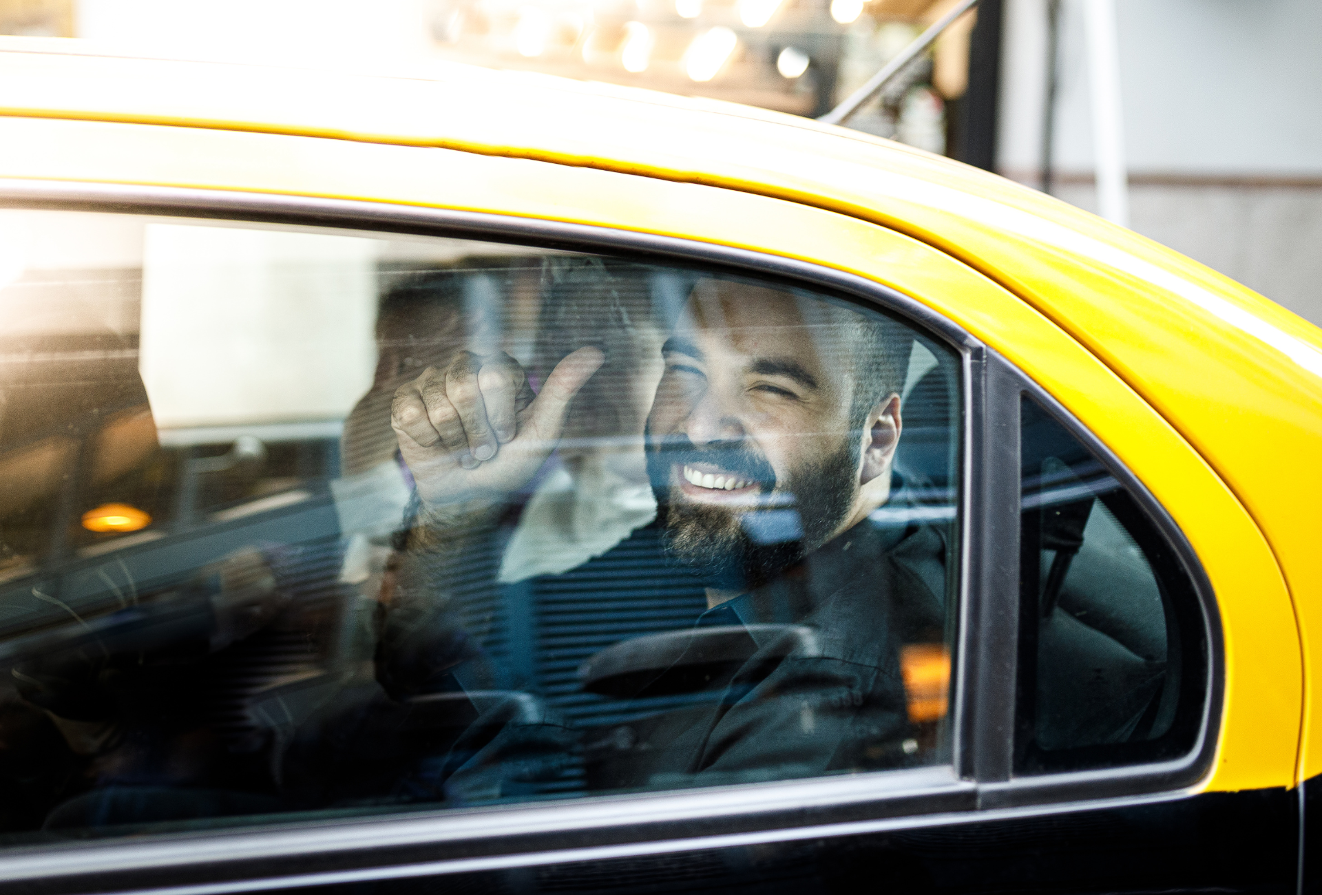 A man is sitting in the back seat of a yellow taxi.