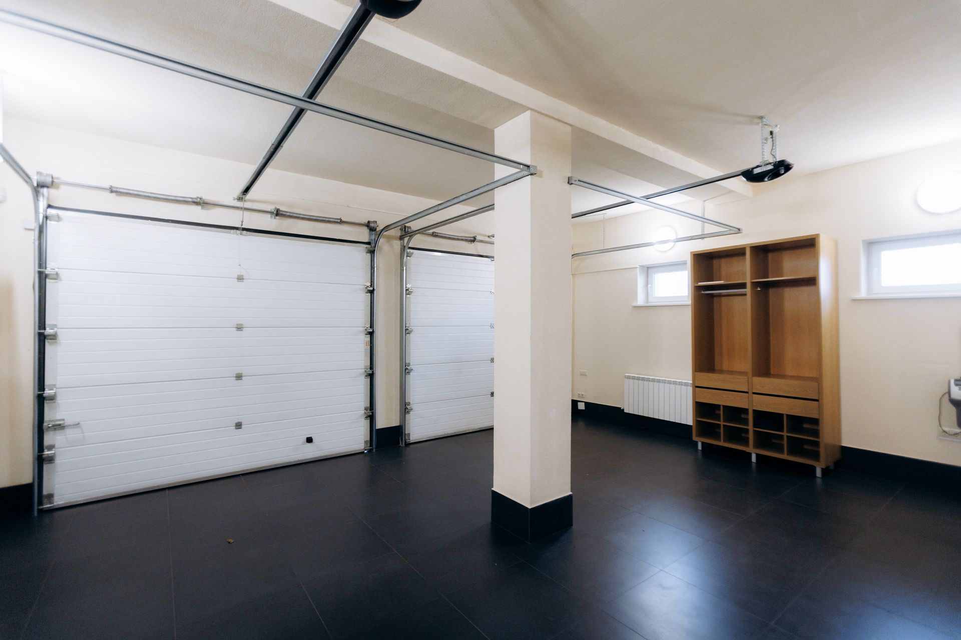 Garage vide avec portes sectionnelles blanches, sol noir et étagères de rangement en bois le long du mur