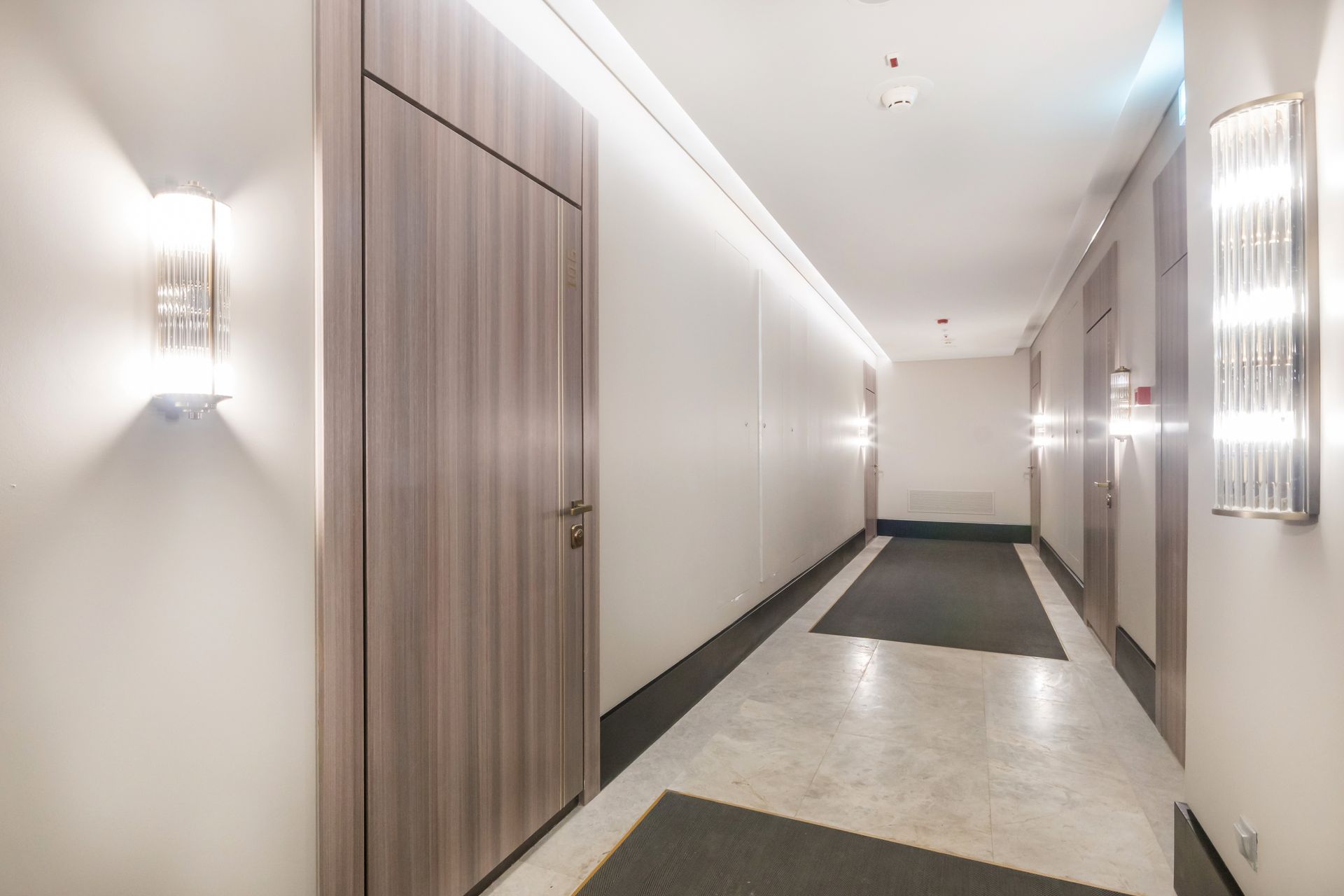 Couloir moderne avec portes en bois, appliques murales et sol en marbre poli