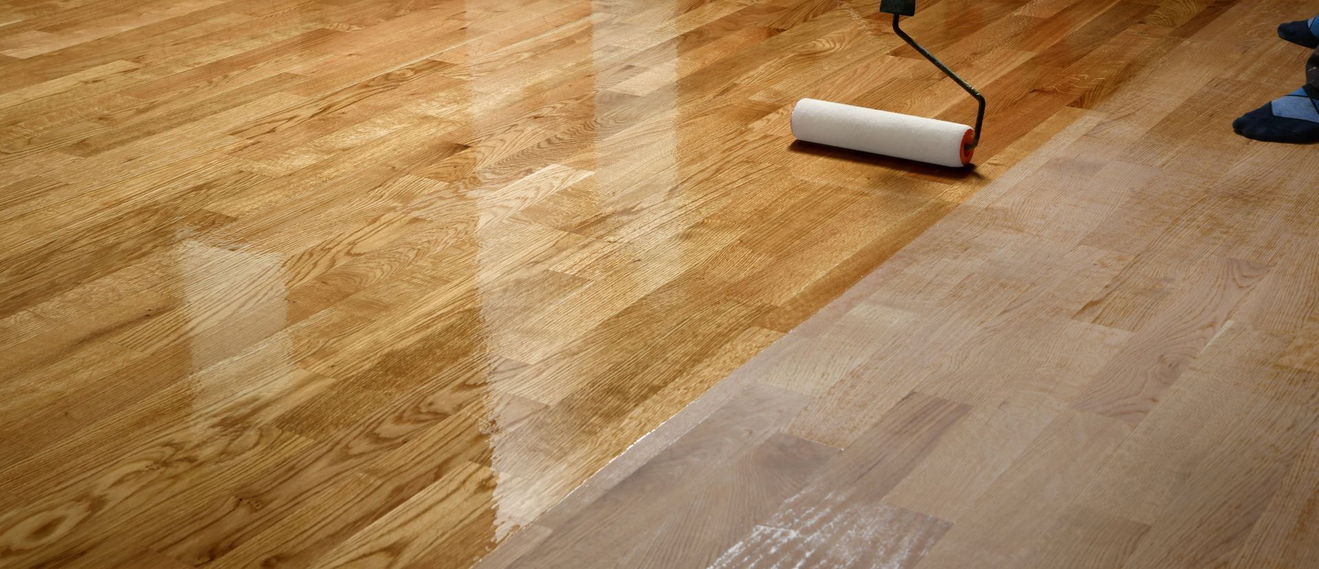 Une personne passe un rouleau à peinture blanche sur un parquet brillant, montrant une finition fraîche.
