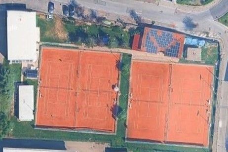 Vista aerea di due campi da tennis in terra rossa circondati da edifici e vegetazione.