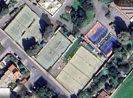 Vista aerea di diversi campi da tennis, alcuni verdi, altri blu, circondati da edifici e vegetazione.