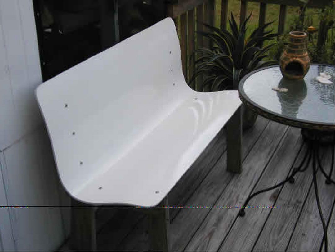 A white bench is sitting on a wooden deck next to a glass table