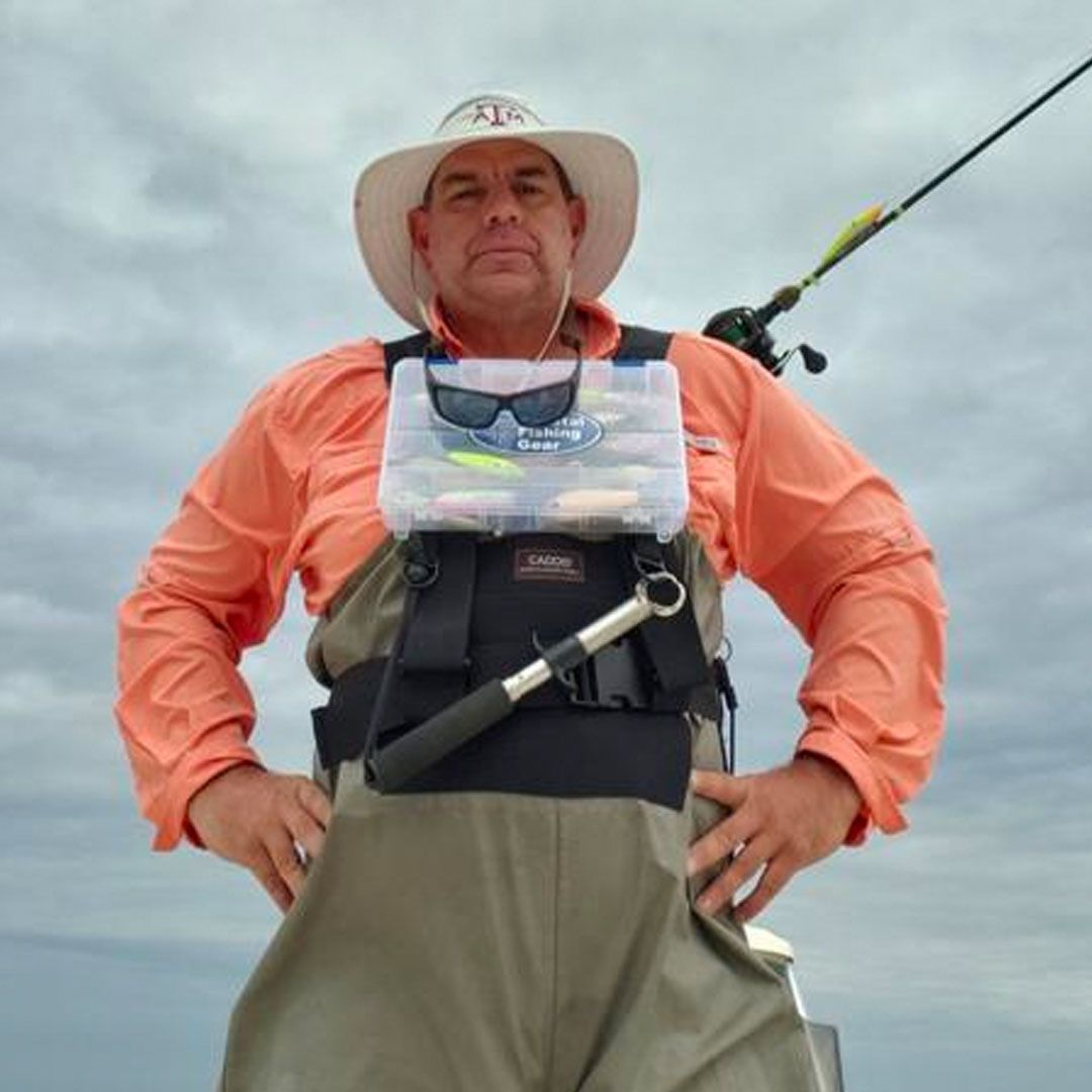 A man wearing a hat and overalls is holding a fishing rod