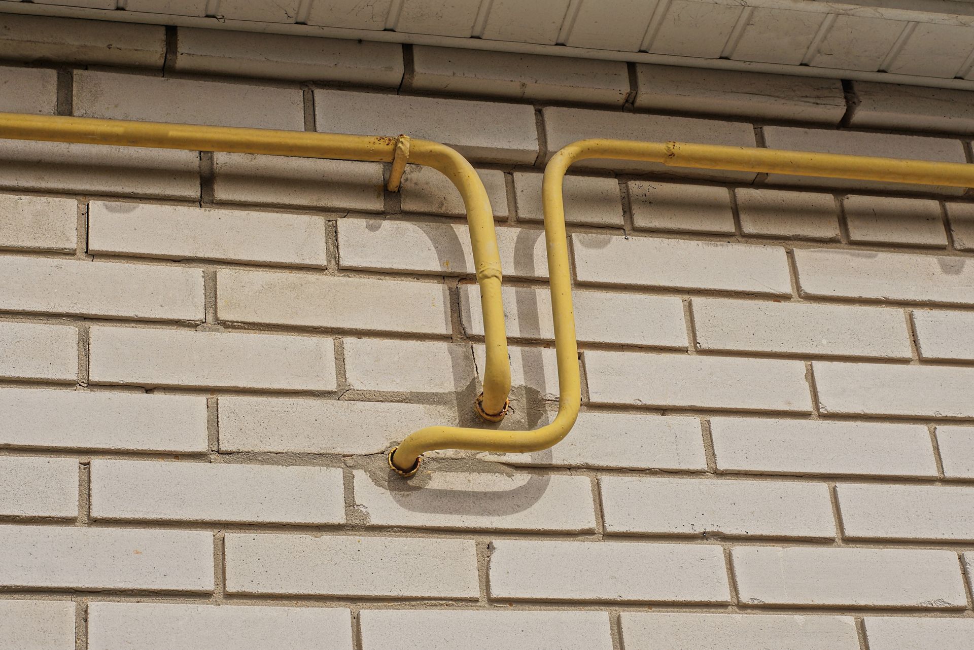 A yellow pipe is attached to a white brick wall