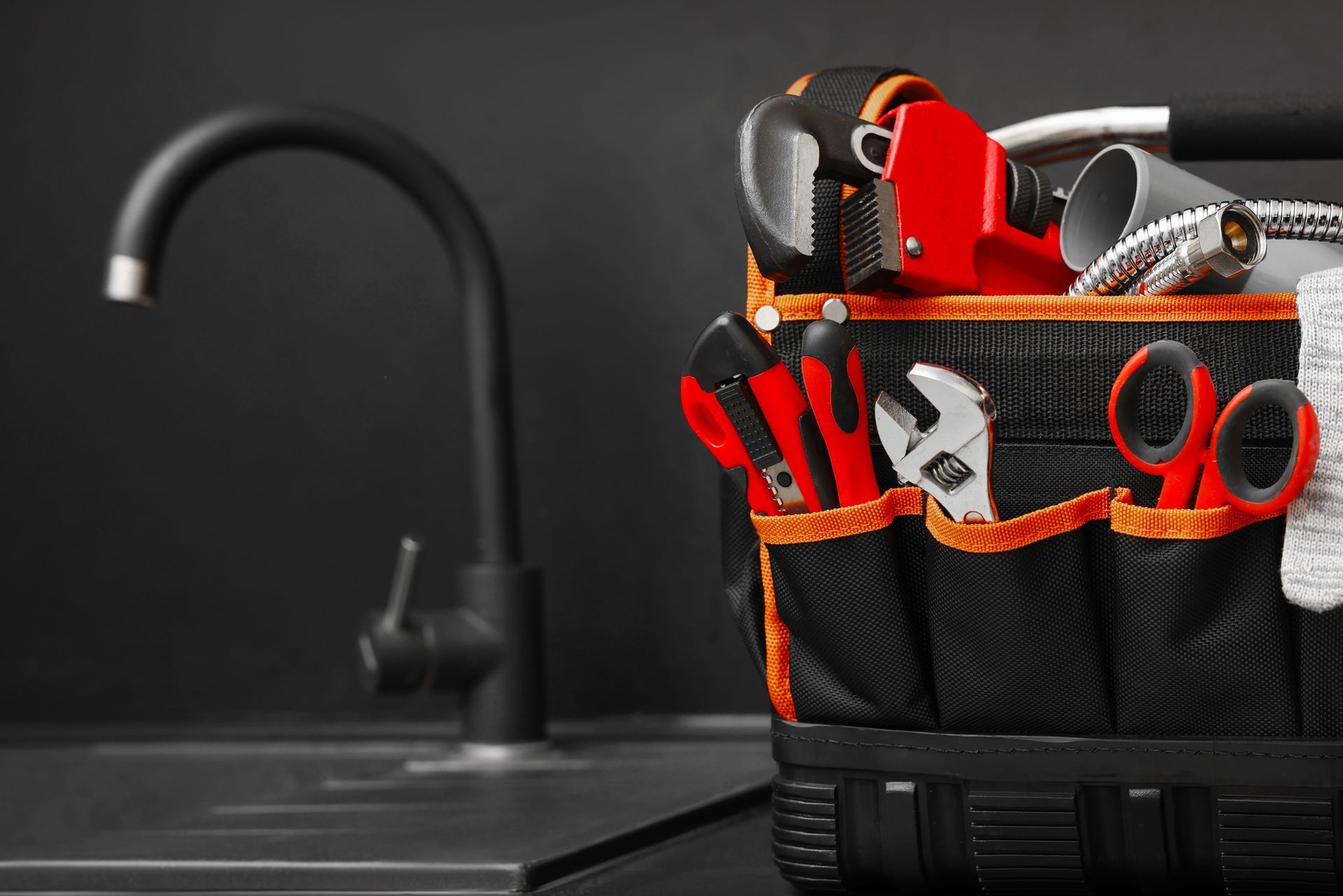 A tool bag filled with plumbing tools is sitting on a counter next to a sink.
