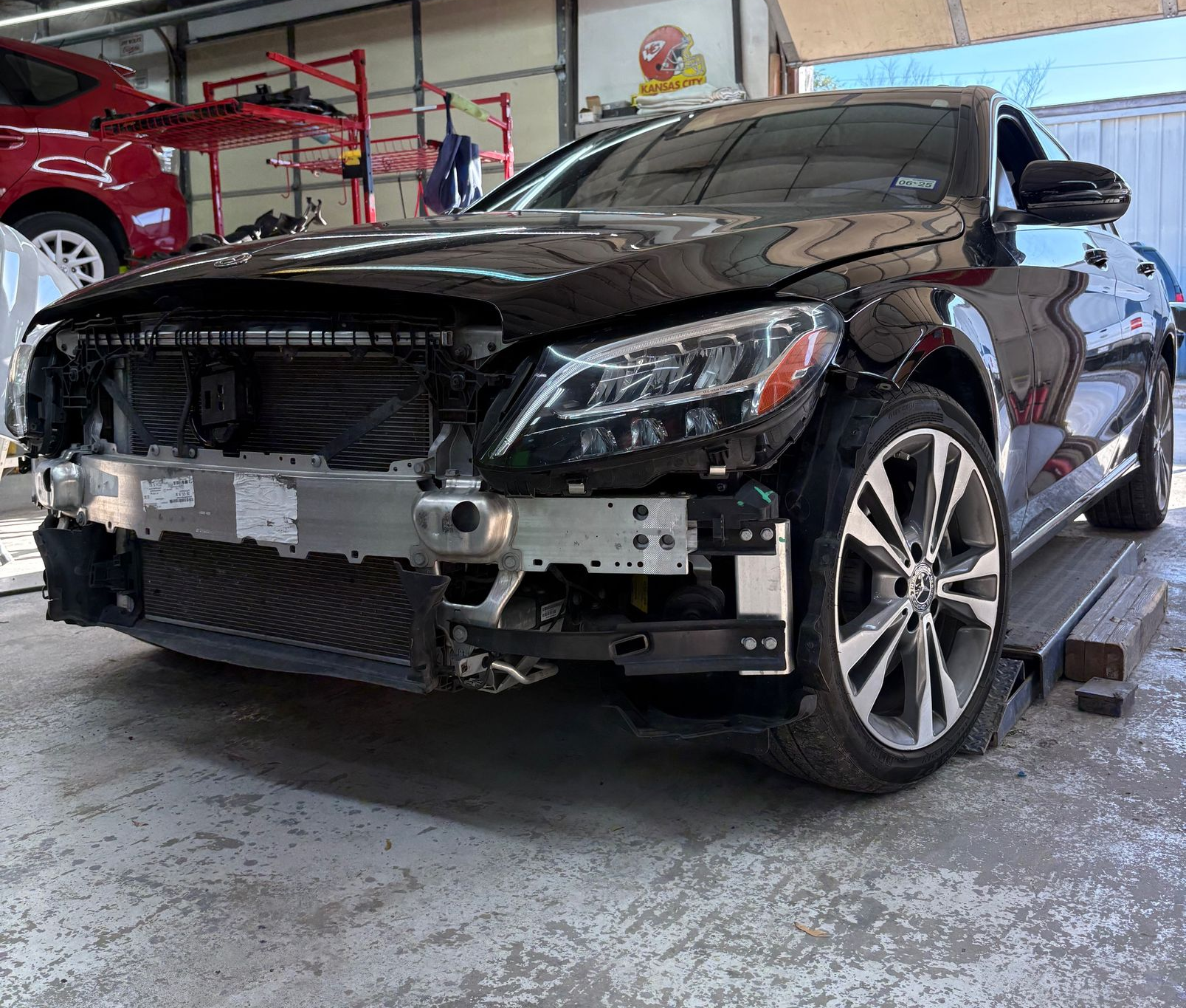 Black car with front bumper removed, in a repair shop.