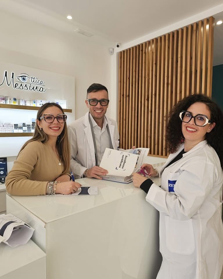Tre professionisti in un negozio di ottica sono seduti dietro un bancone e sorridono mentre esaminano insieme i documenti.