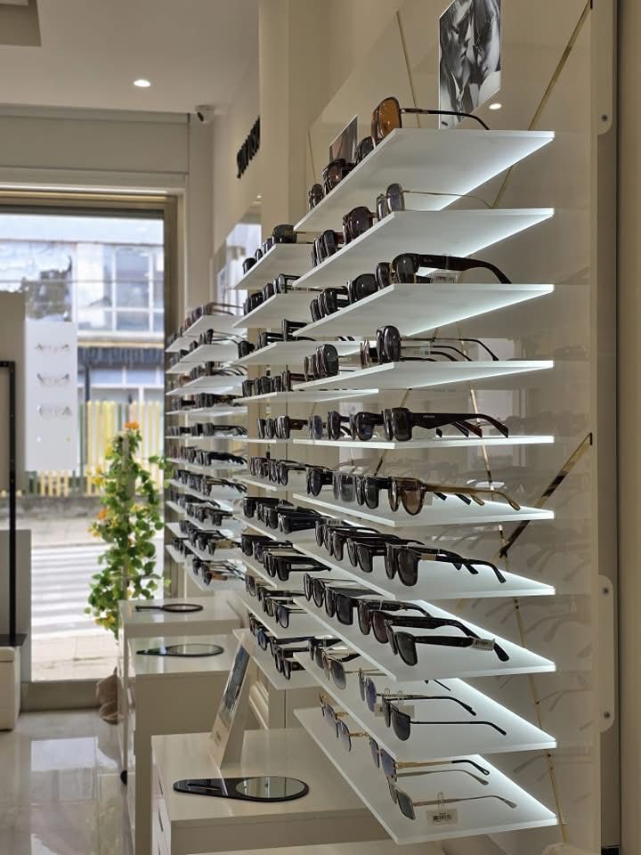 Diversi scaffali su una parete espongono numerosi occhiali da sole in un negozio di ottica moderno e luminoso.