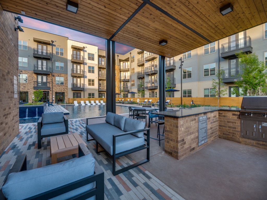 A patio area with a couch , chairs , tables and a grill.
