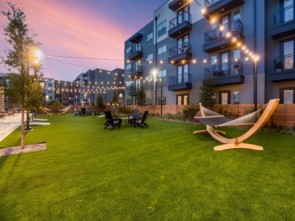 A hammock is sitting on top of a lush green lawn in front of a building.