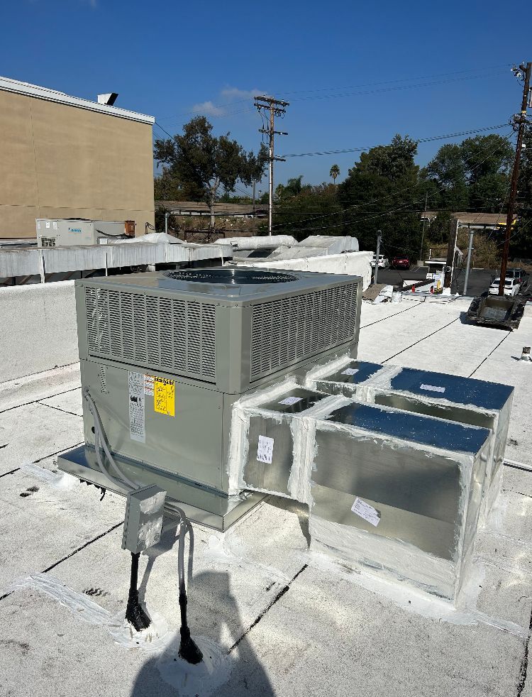 An HVAC unit on a flat roof with ductwork, against a blue sky, in daylight.