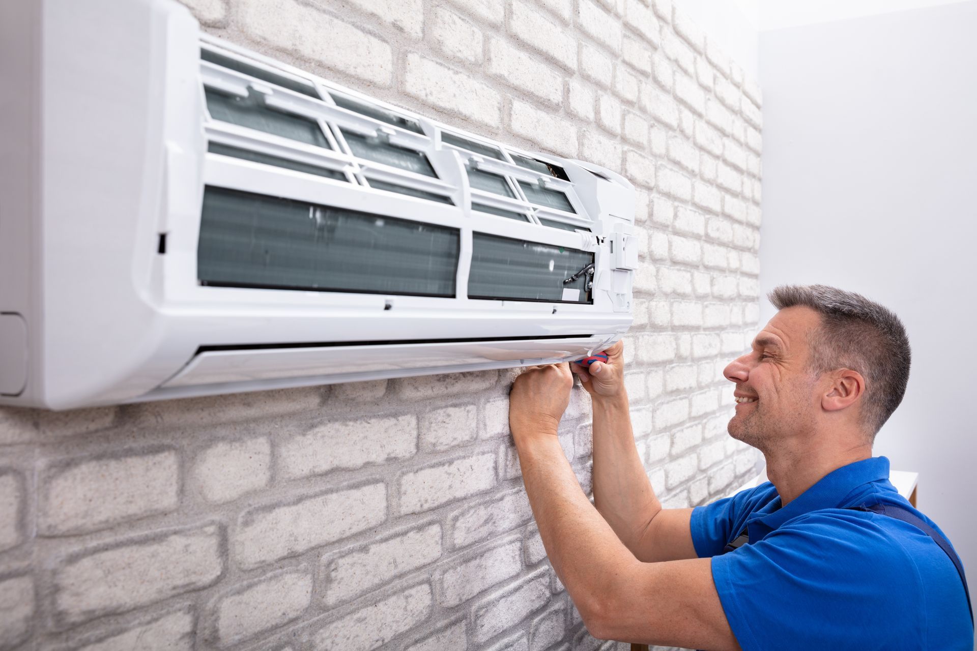 Man in blue shirt, installing an air conditioner on a brick wall.