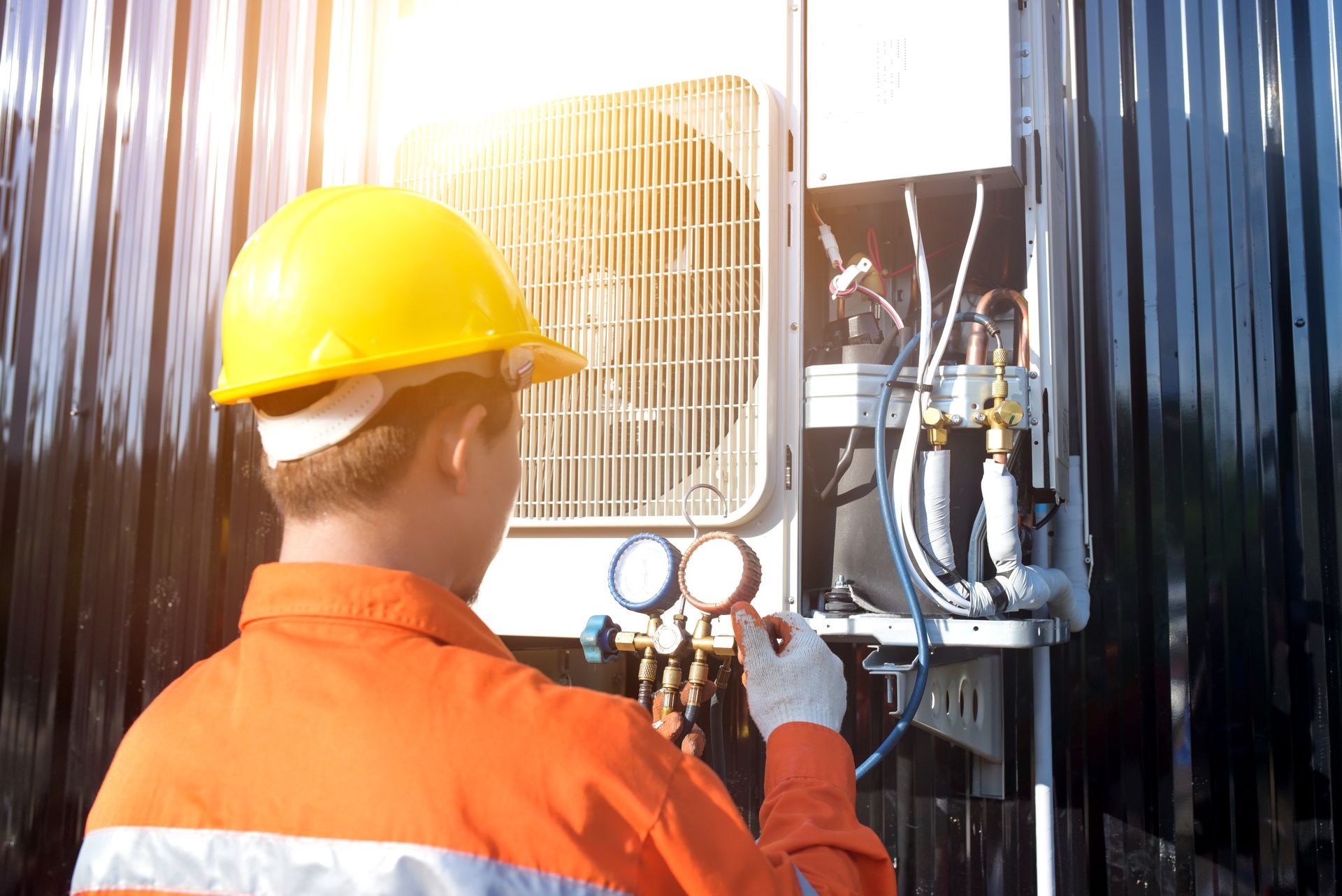 HVAC technician in orange uniform and hard hat checks AC unit with gauges outdoors.