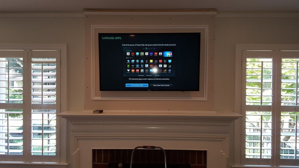 Living room wall with a mounted TV above a fireplace, flanked by windows with shutters.