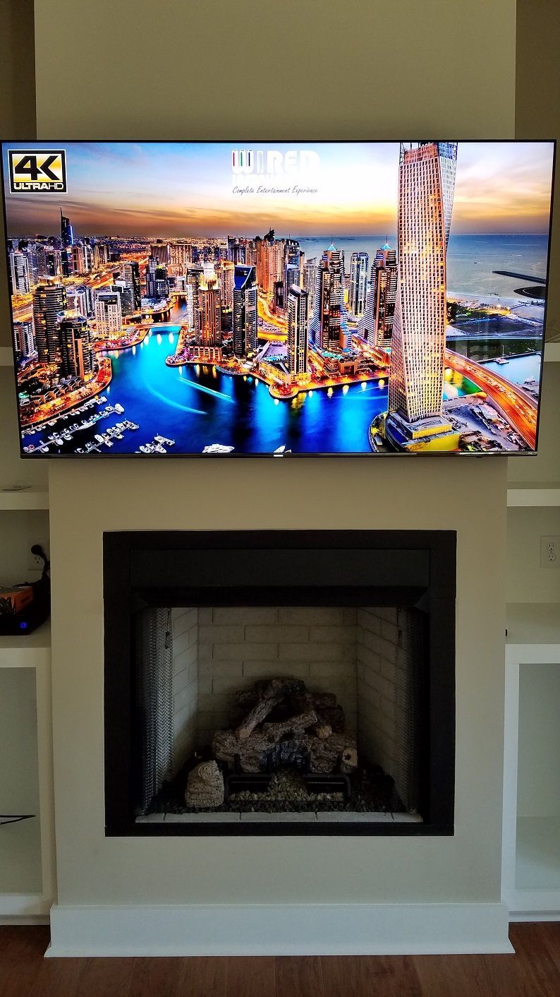 Wall-mounted TV above a black fireplace, showing a colorful city skyline at night.