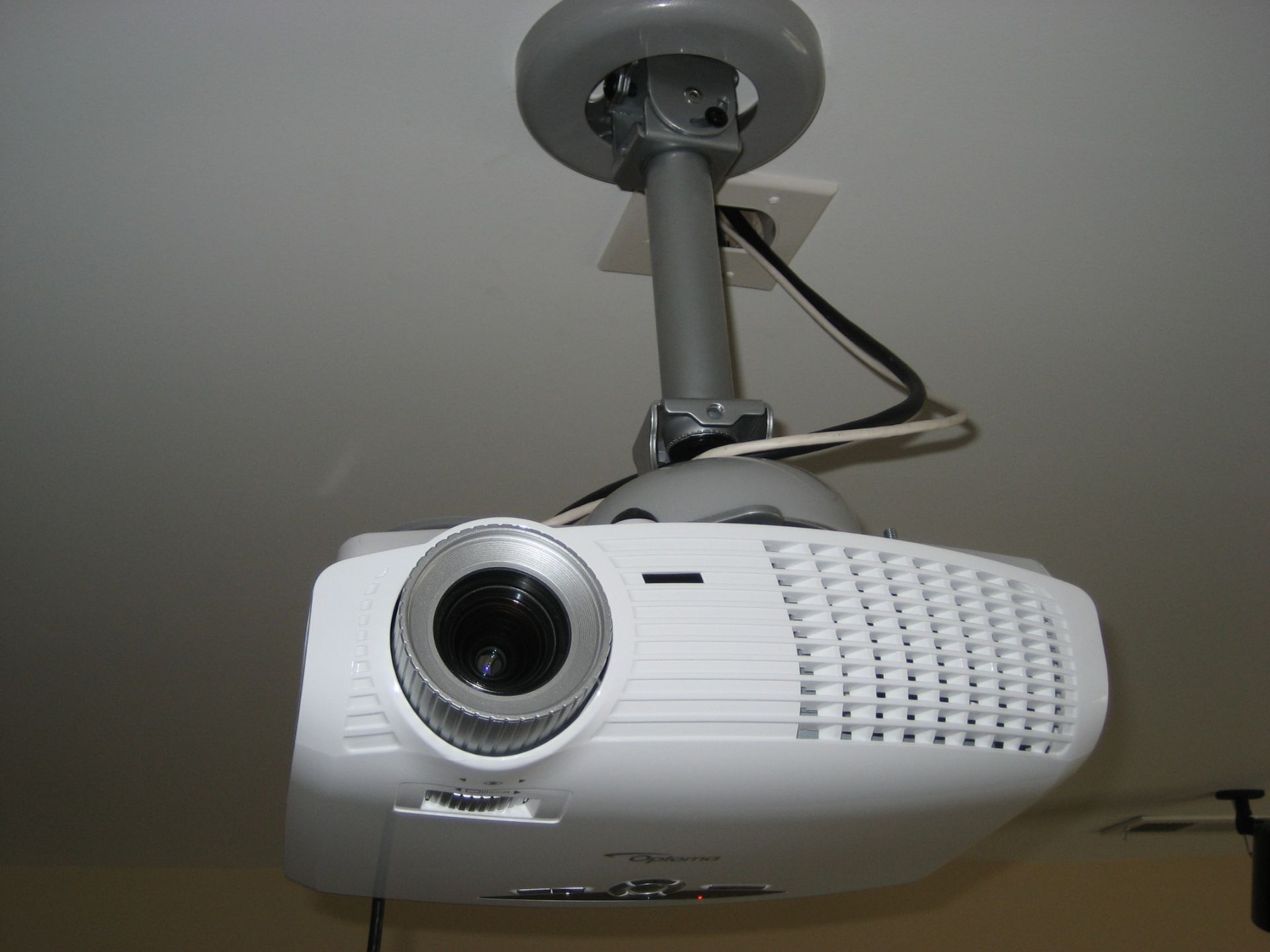 Ceiling-mounted white projector hanging from a mount with a visible cable