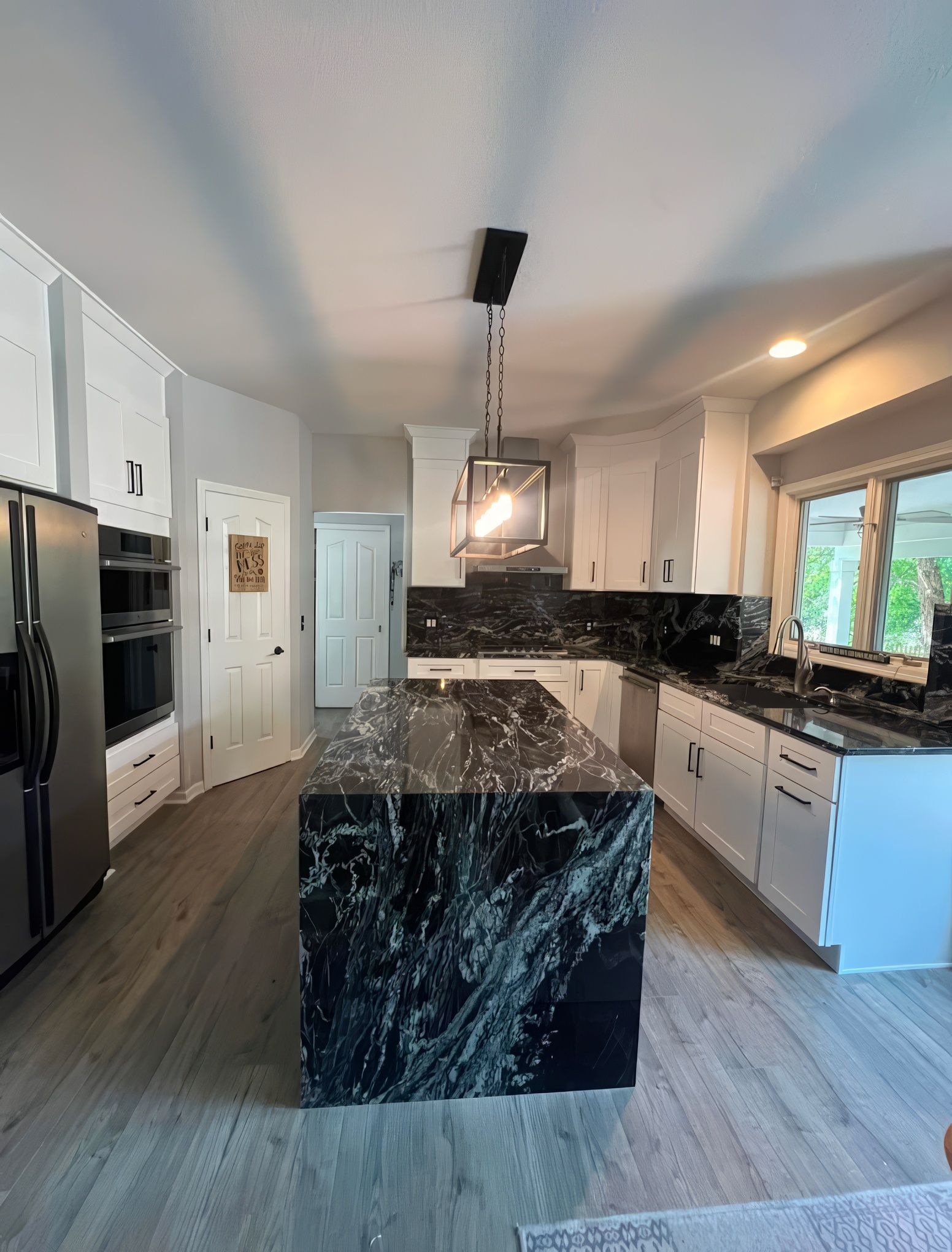Modern kitchen with a black and white granite island, white cabinets, and stainless steel appliances.