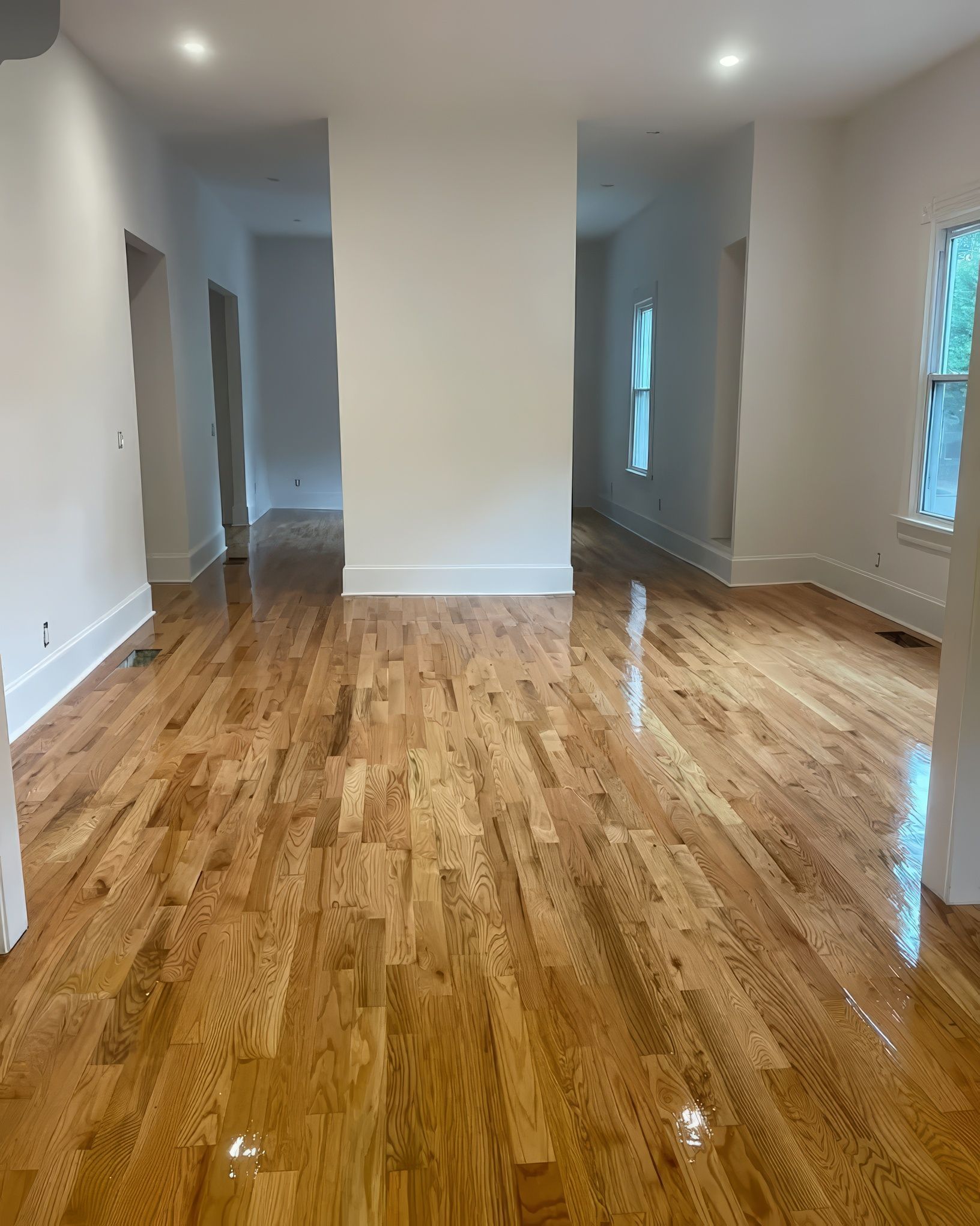 Hardwood floor, white walls, and bright lighting in an empty room, leading to doorways.