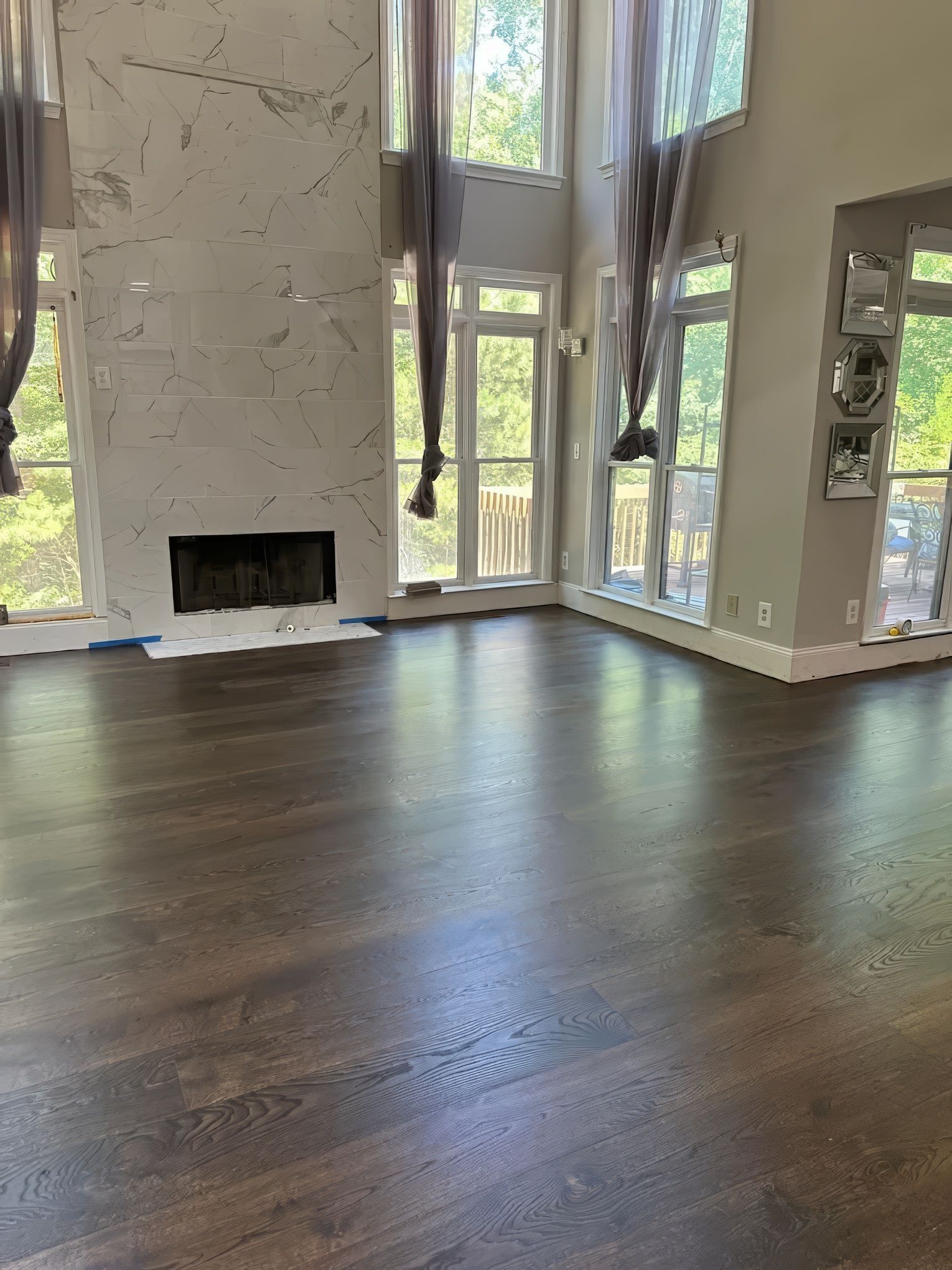 Dark wooden floors in a room with large windows, fireplace, and mirrors. Natural light floods the space.