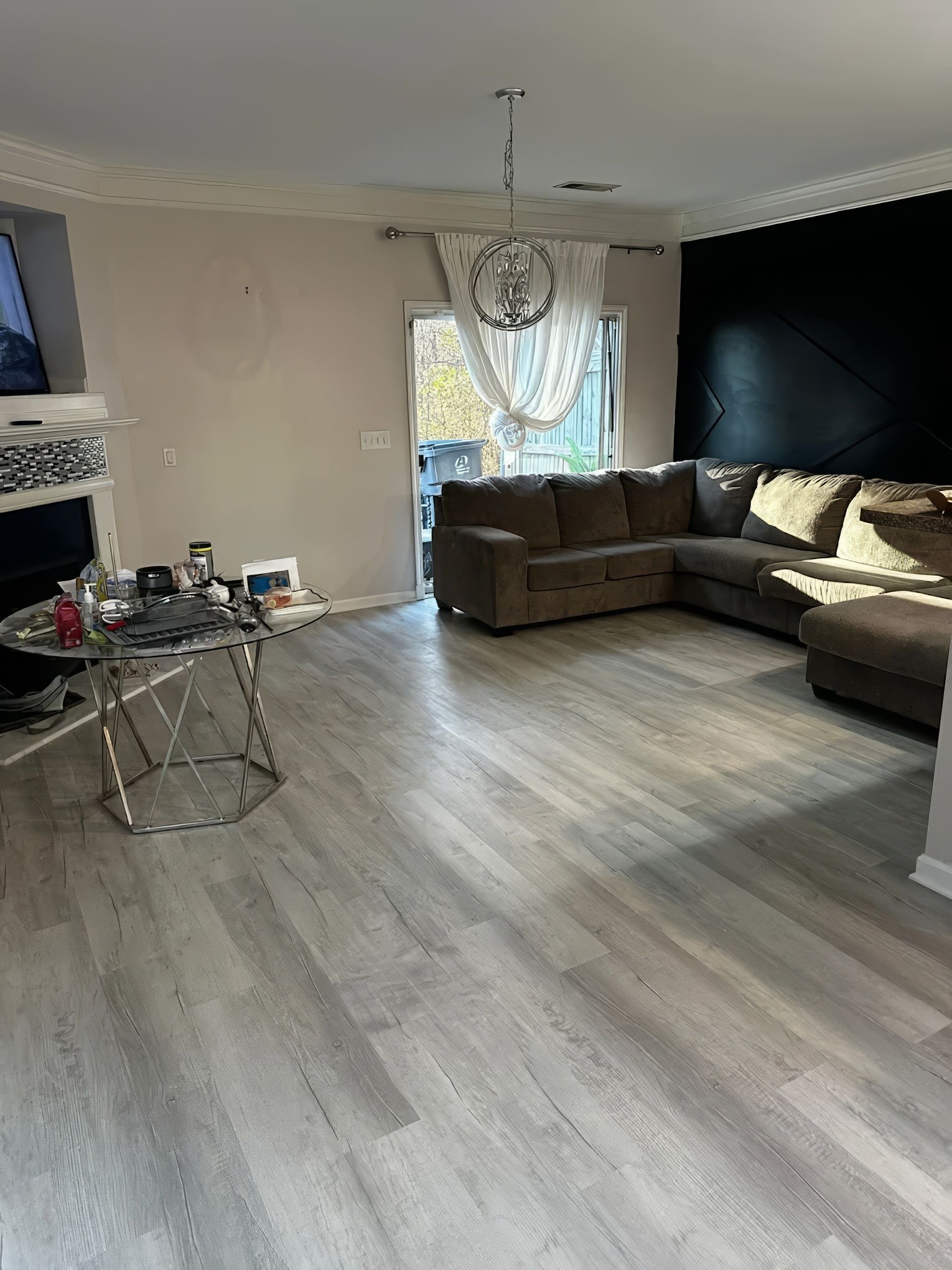 Living room with gray wood floors, a brown sectional sofa, and a black accent wall.