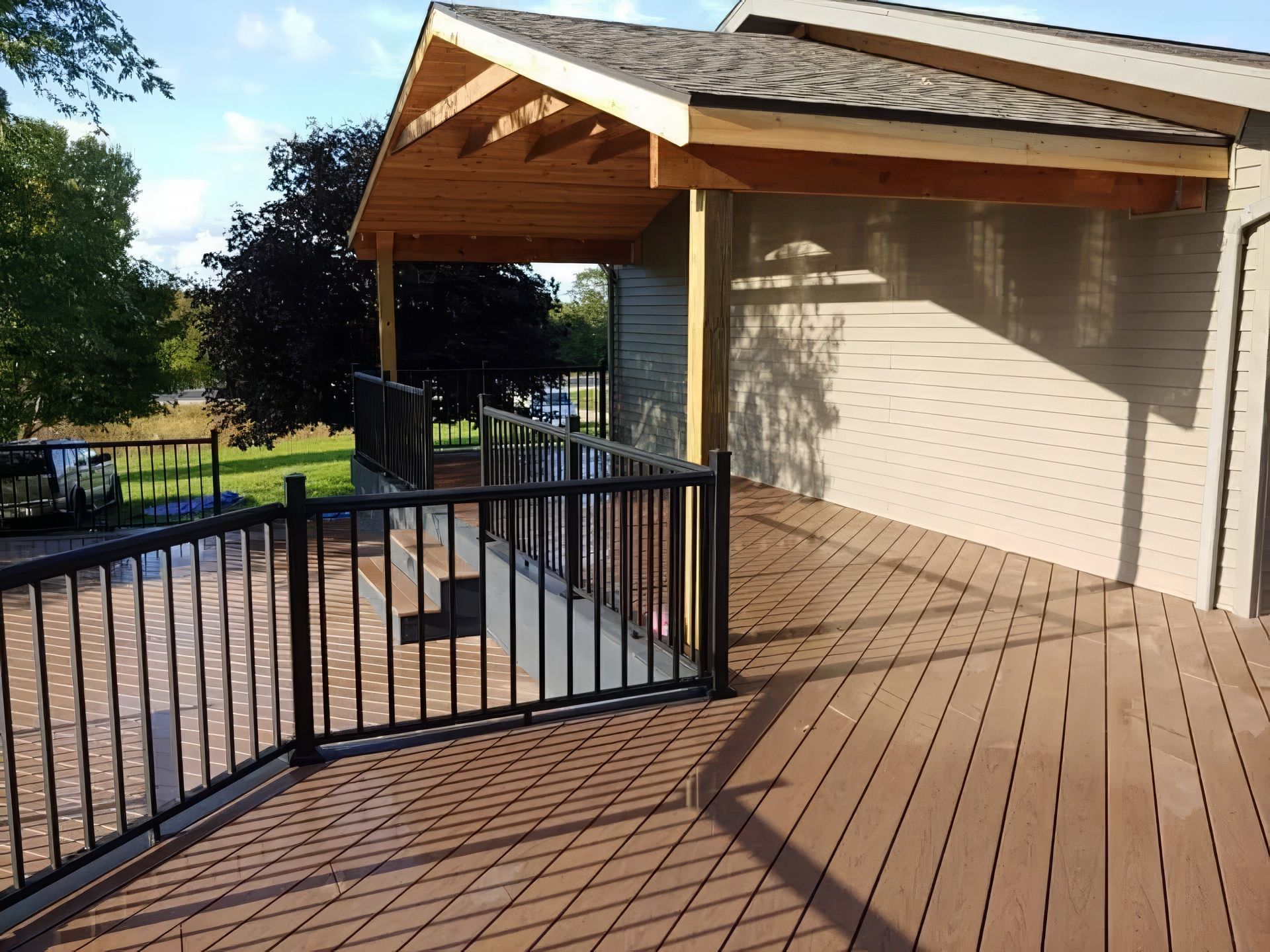 Deck with black railing, brown composite decking, and covered area with wooden beams.