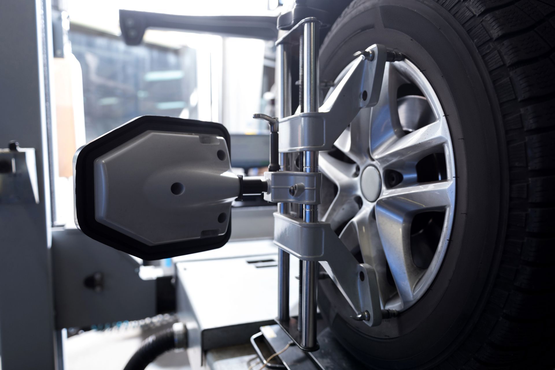 A close-up view of an automotive wheel alignment sensor mounted to a car tire in an auto repair shop.