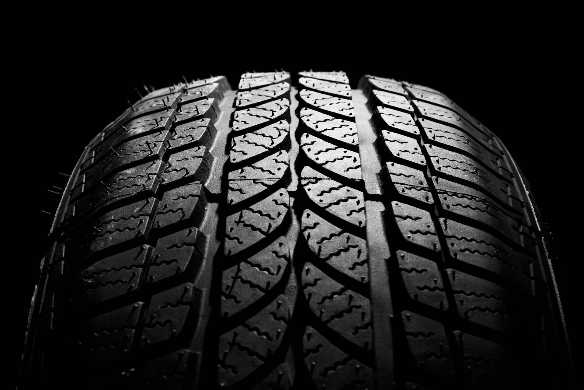 Close-up of a black car tire tread, illuminated from the side against a dark background.