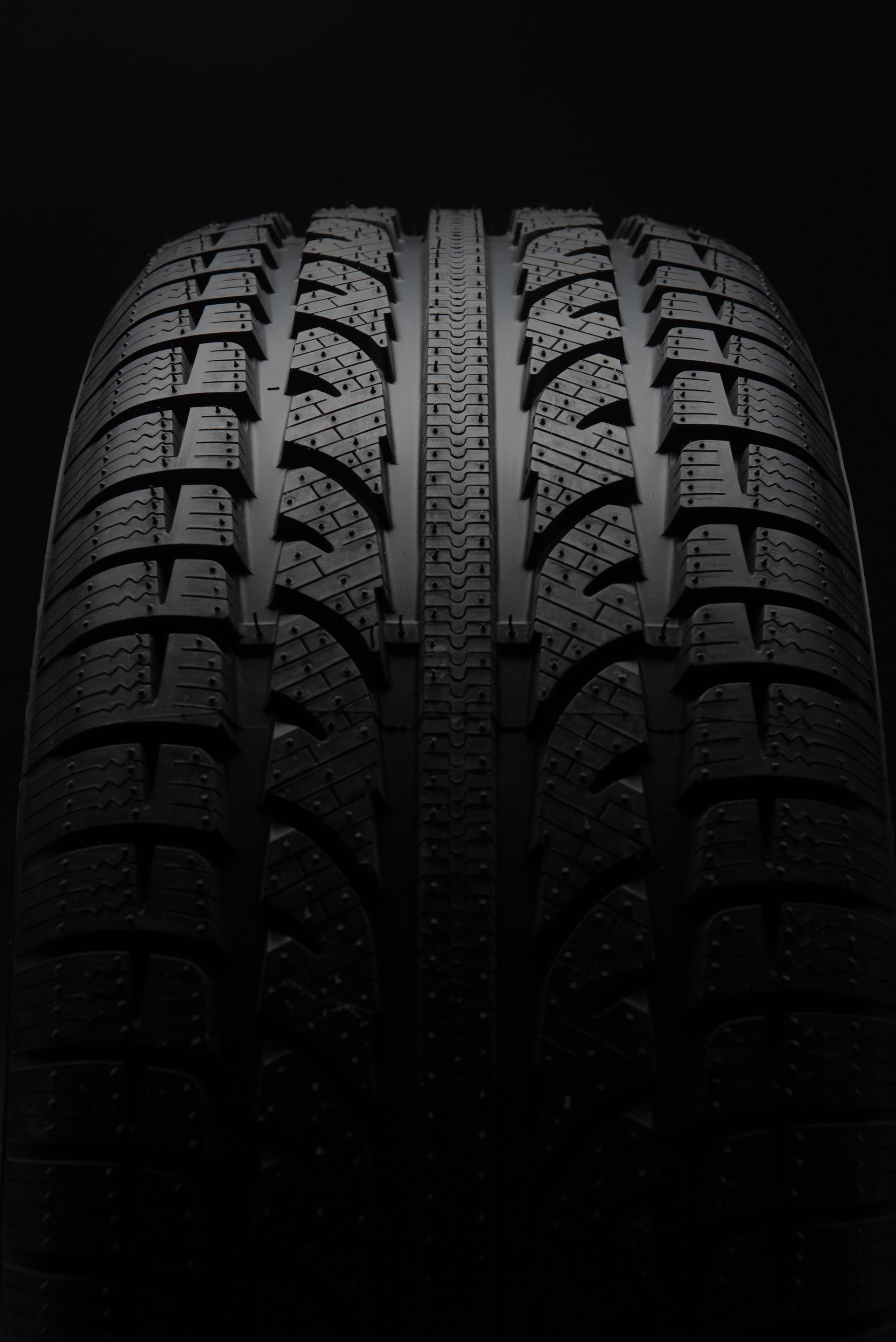 A close-up, front-facing view of a black tire with a symmetrical, aggressive tread pattern against a dark background.