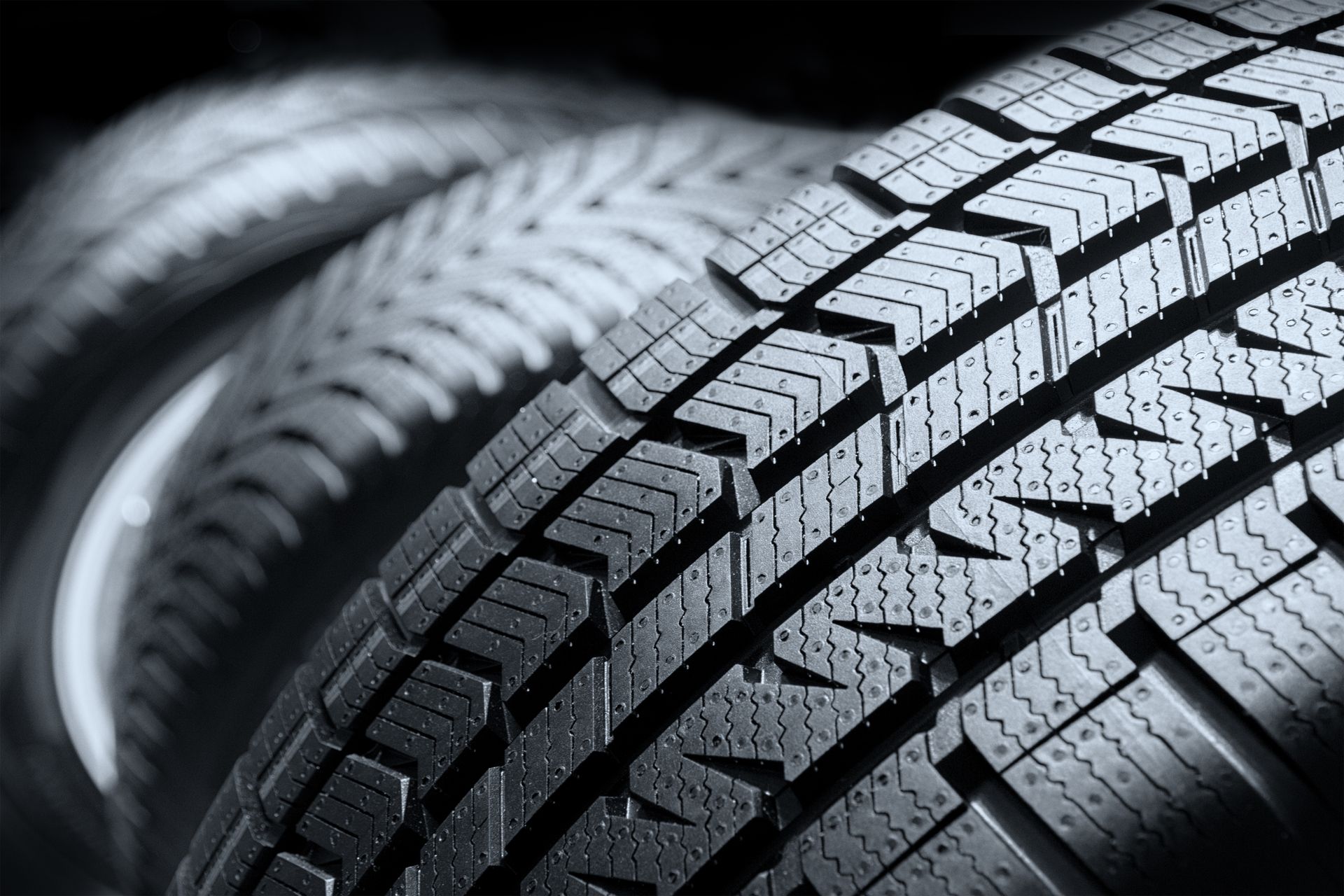 A close-up, angled view of a black car tire with a distinct chevron-patterned tread design.