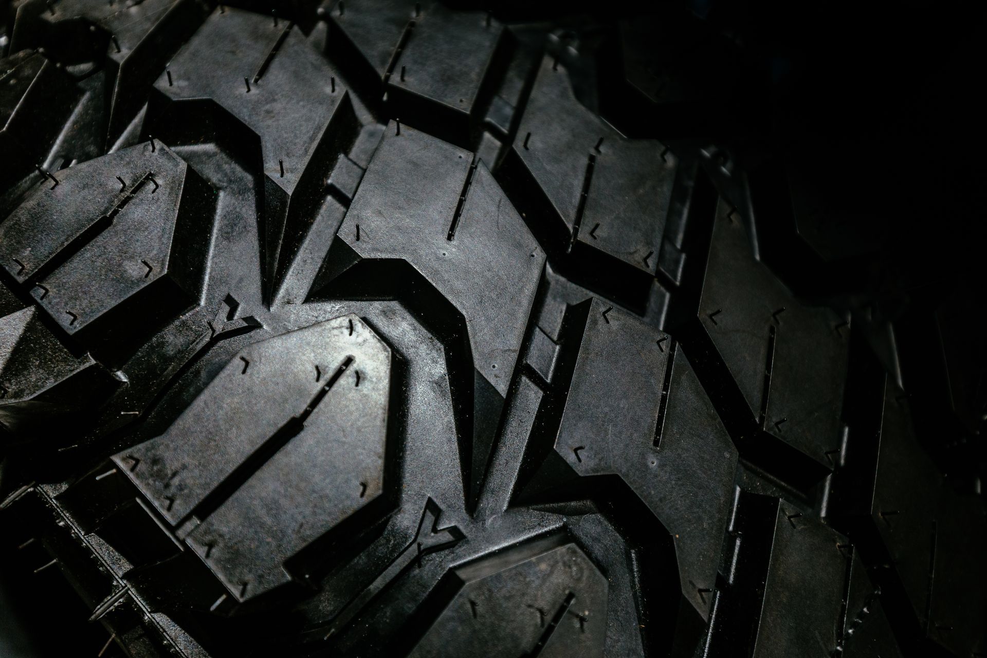 A close-up, high-angle shot of a black, rugged off-road tire with deep, aggressive treads and sharp patterns.
