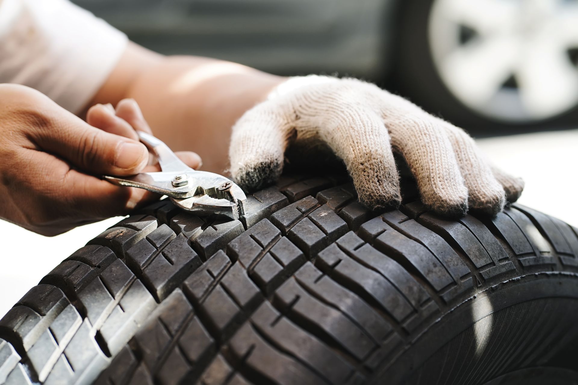 A mechanic uses pliers to remove a nail embedded in the tread of a car tire.