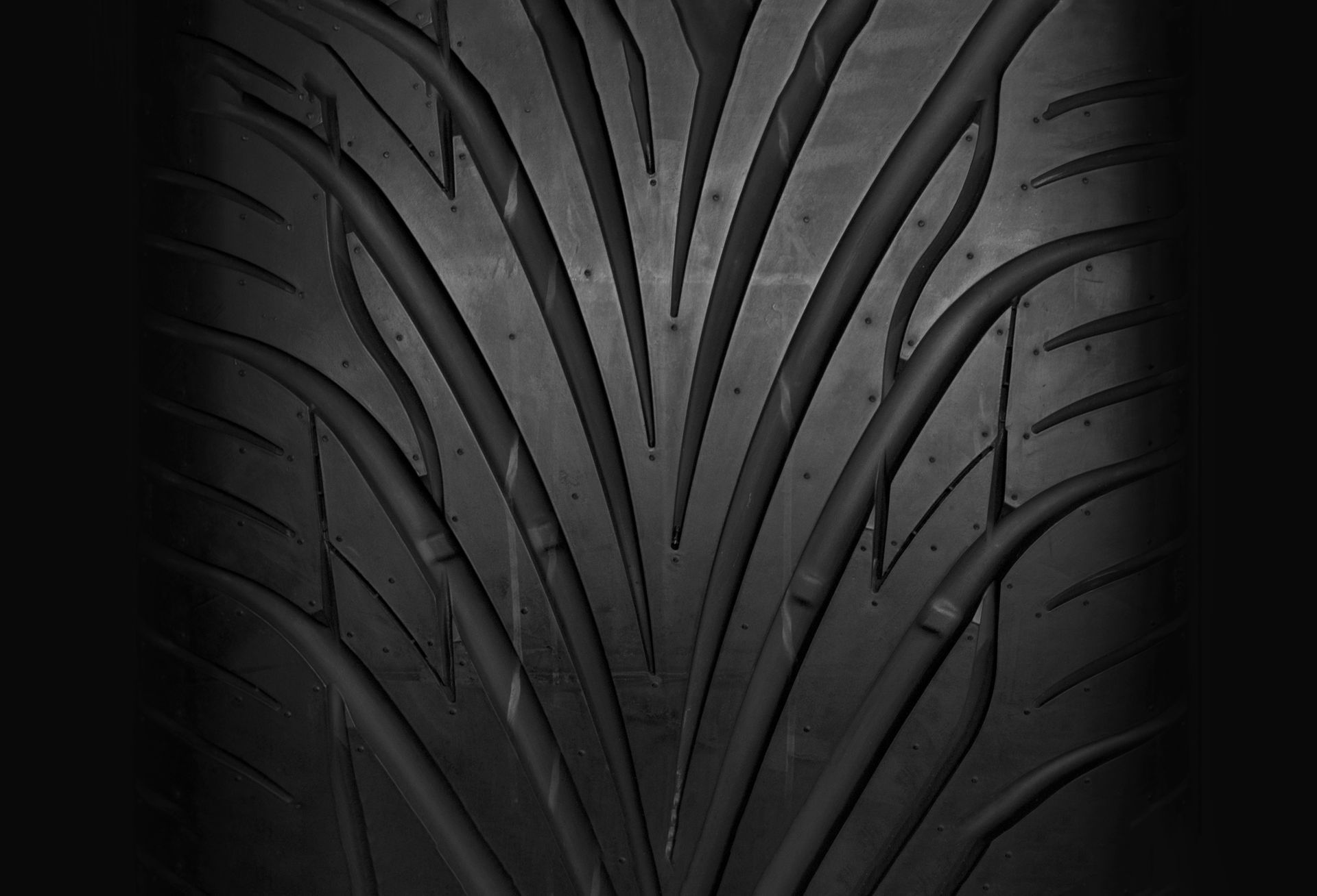 A close-up, top-down view of a black tire with a directional V-shaped tread pattern designed for water evacuation.