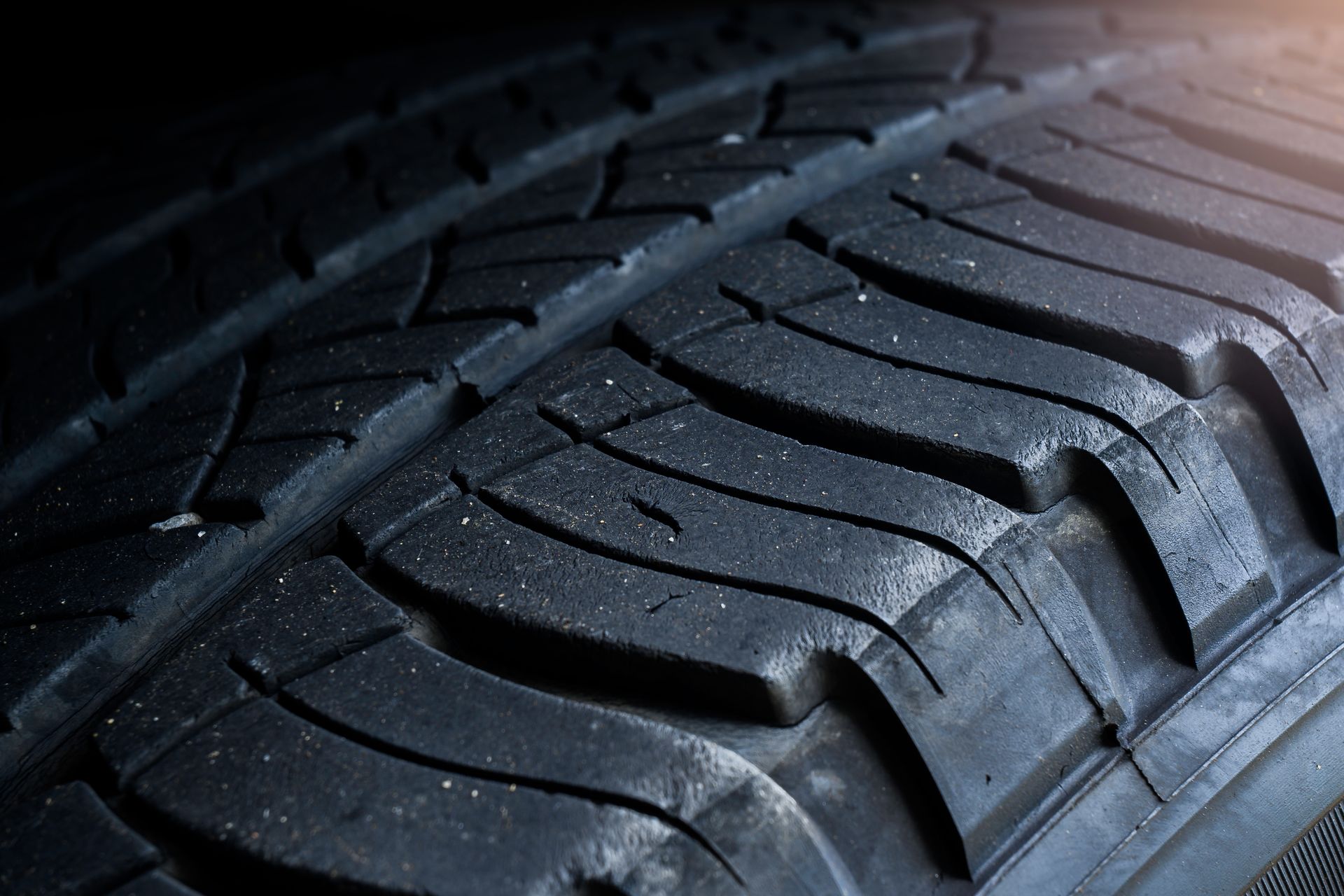 Close-up of a dark, worn car tire showing the patterned rubber tread.