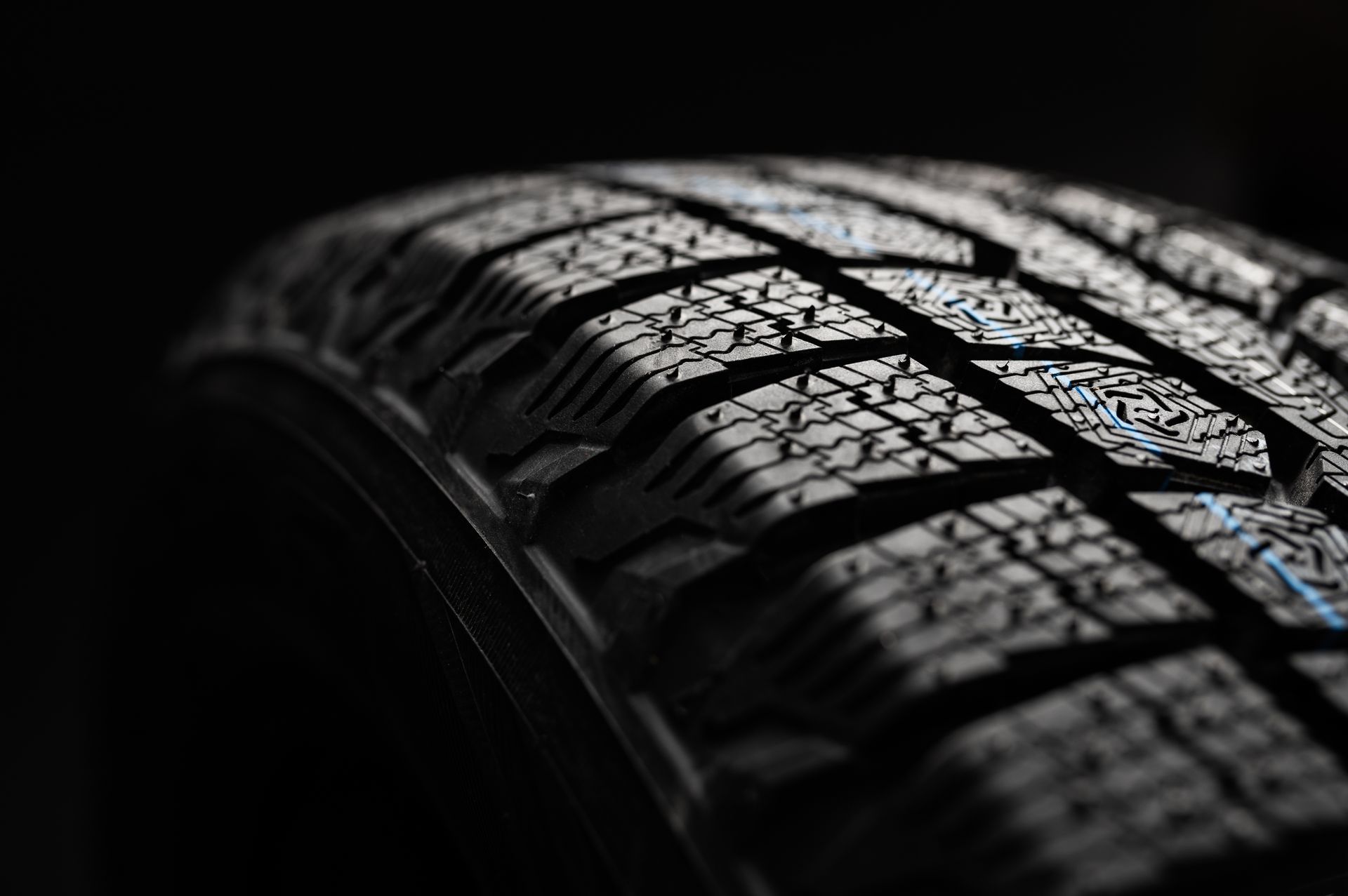 Close-up of a black tire with a deep, textured winter tread pattern against a dark background.