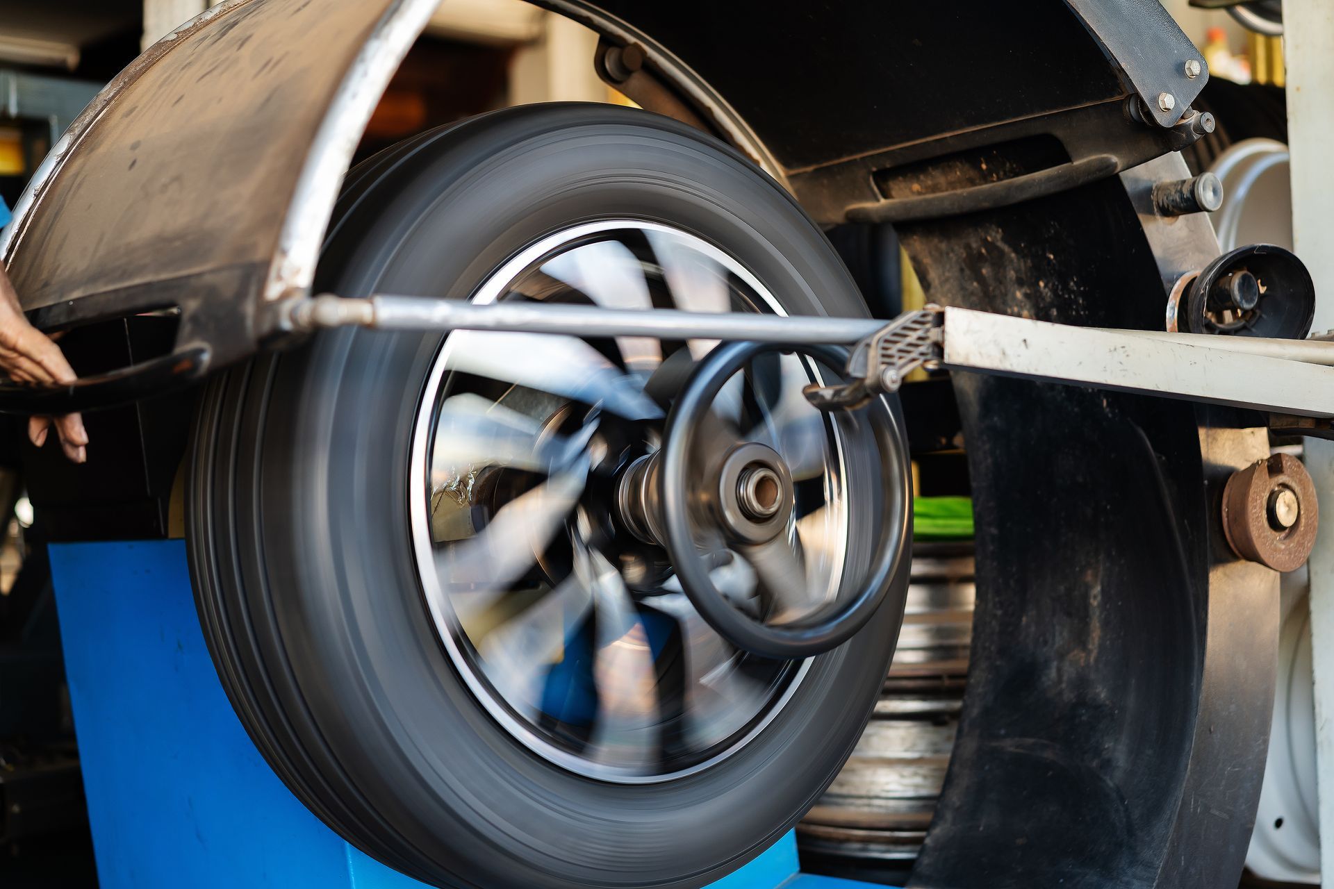 A car wheel and tire mounted on a spinning wheel balancing machine inside a garage.