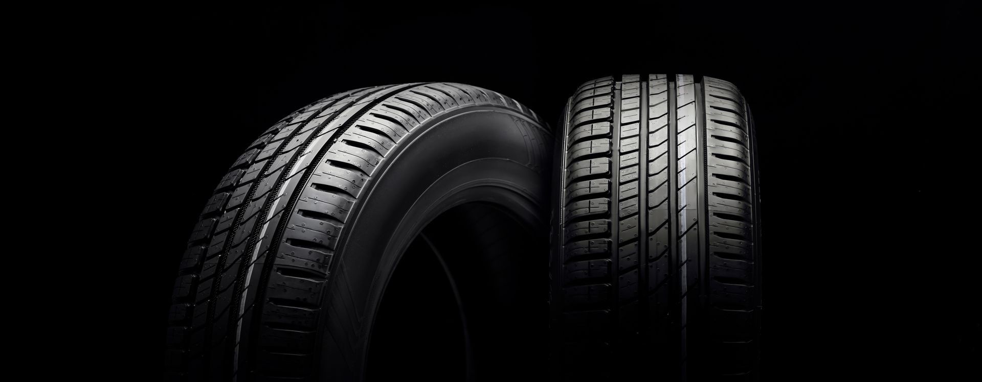 Two black tires standing against a dark, minimalist background.