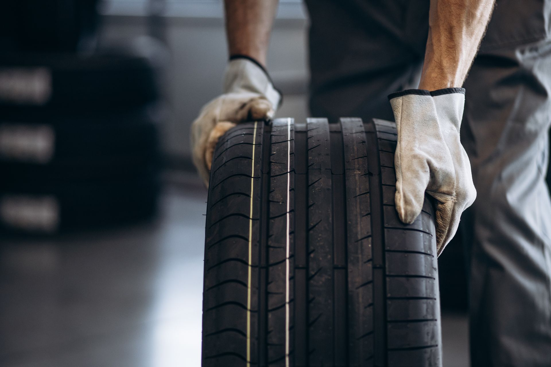 A worker in work clothes and gloves holds a new tire in an auto shop.