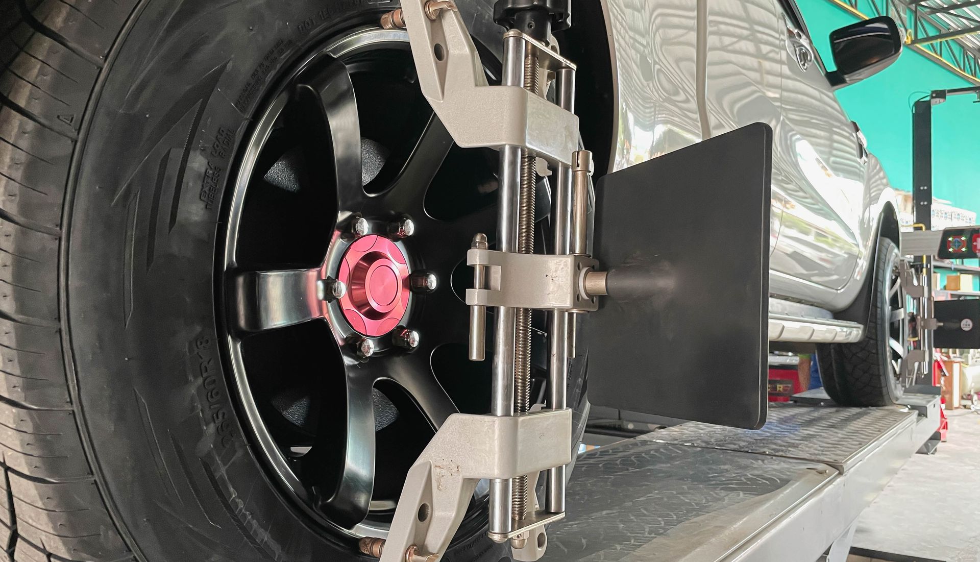 A wheel alignment sensor clamped to a black car wheel on an automotive lift in a workshop.