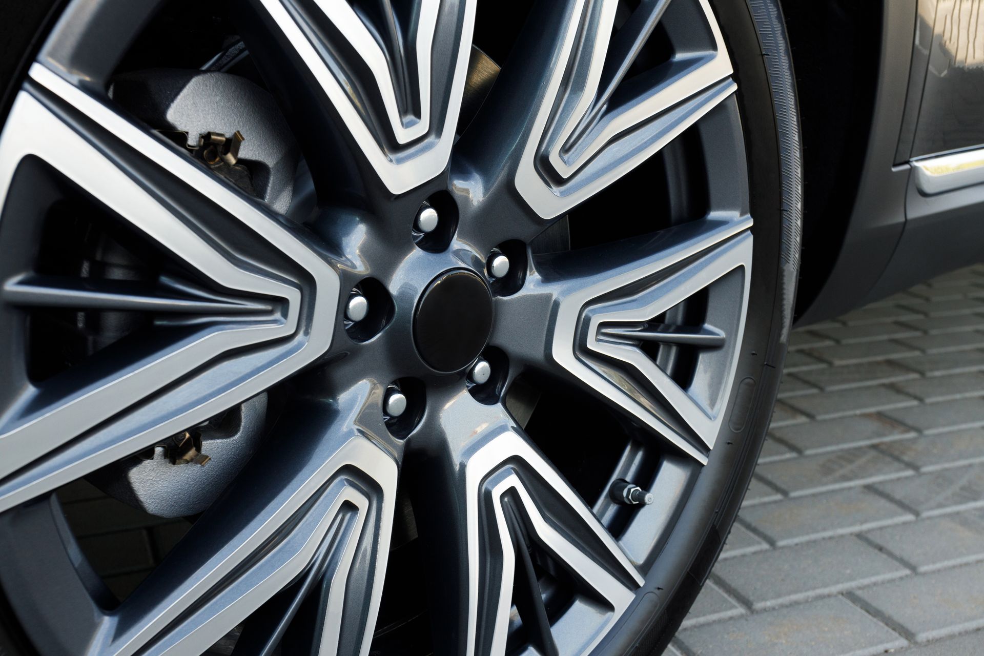 Close-up of a modern, multi-spoke dark grey and silver alloy wheel on a vehicle parked on paved ground.