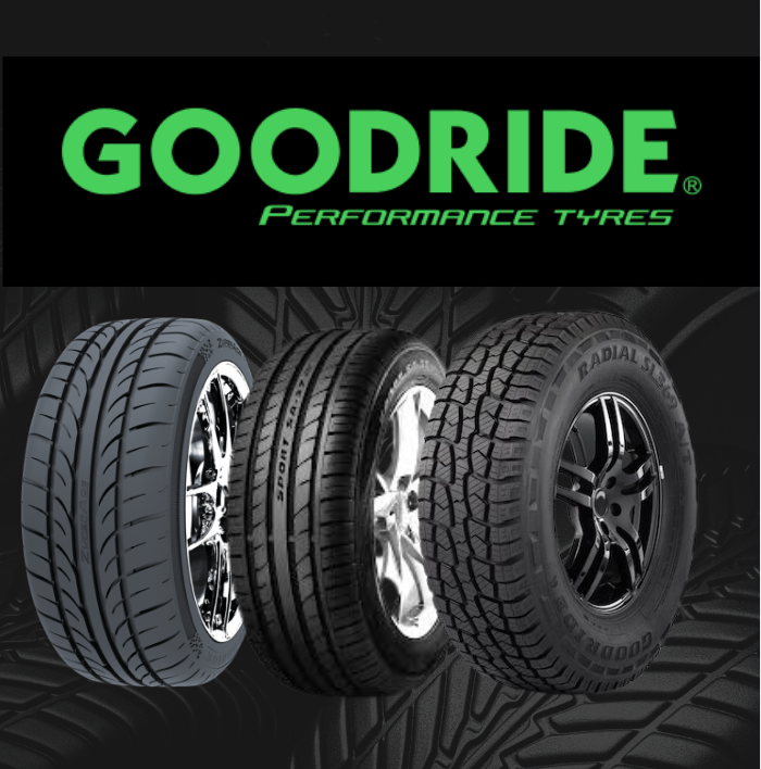 Hands wearing black and red work gloves hold a winter tire with a directional tread pattern against a black background.