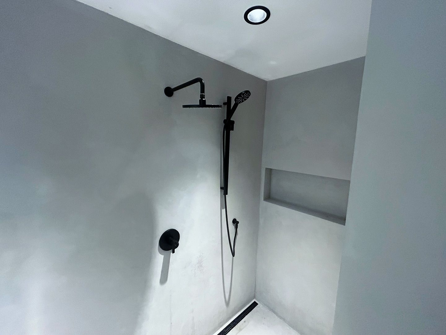 A shower with a black shower head and a black hose in a bathroom.