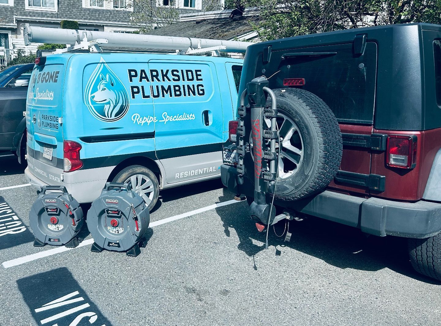 A parkside plumbing van is parked next to a red jeep in a parking lot.