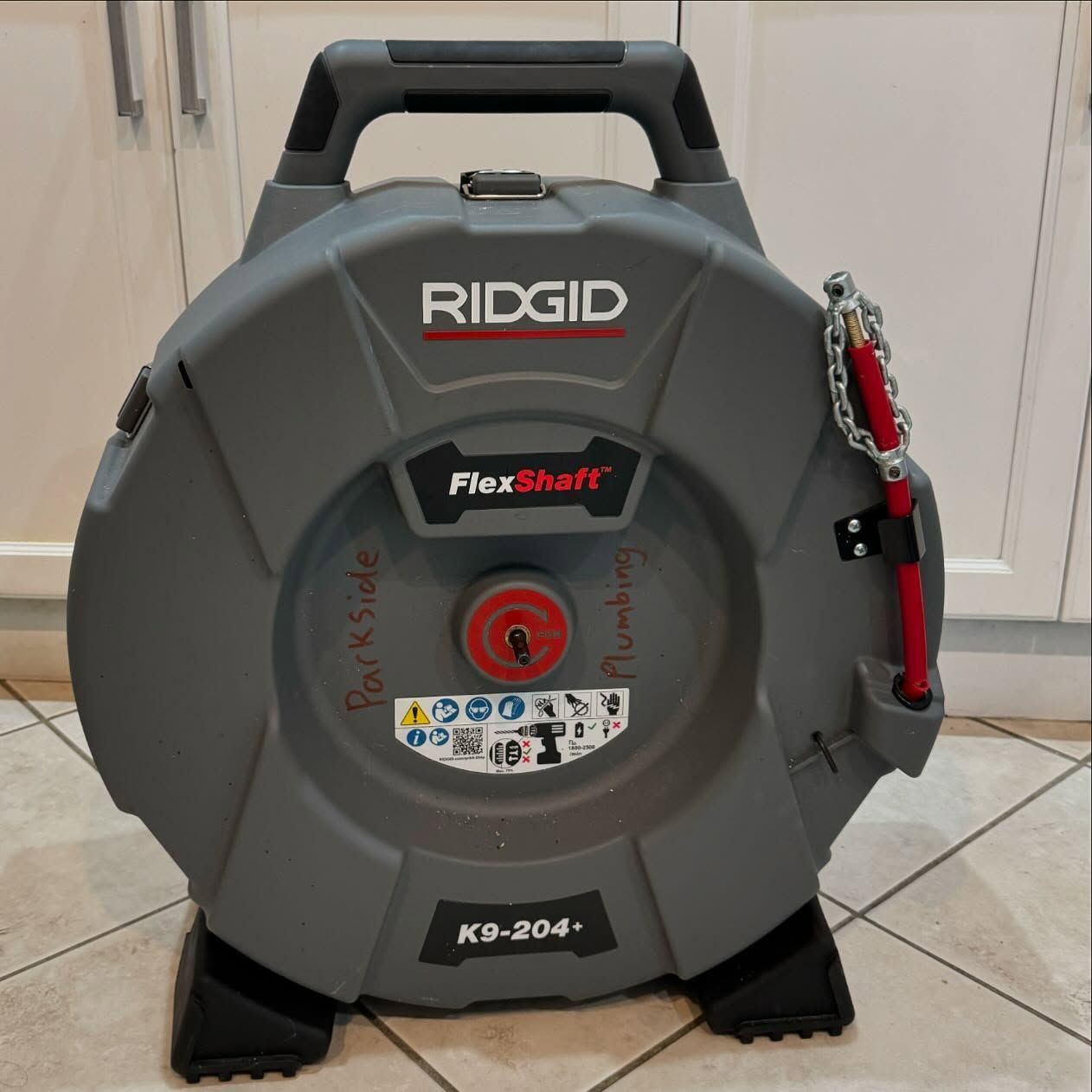 A ridgid flexshaft drain cleaner is sitting on a tiled floor