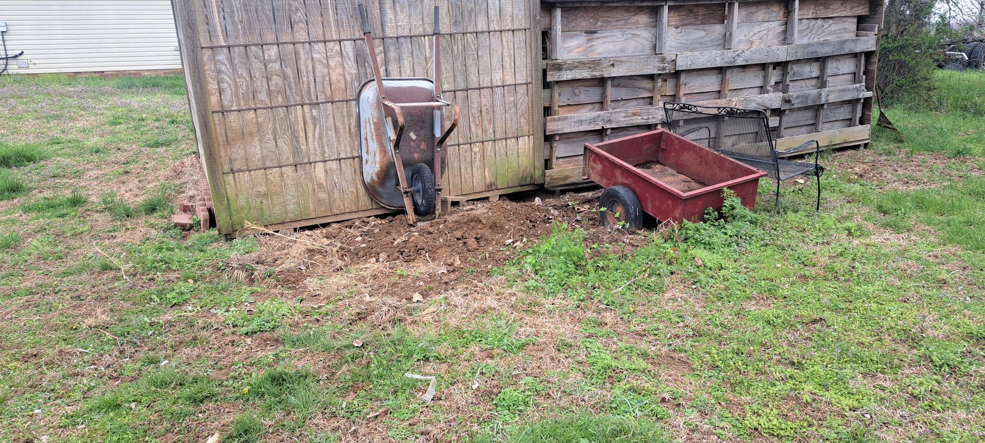 A red wheelbarrow is sitting in the grass next to a wooden shed.