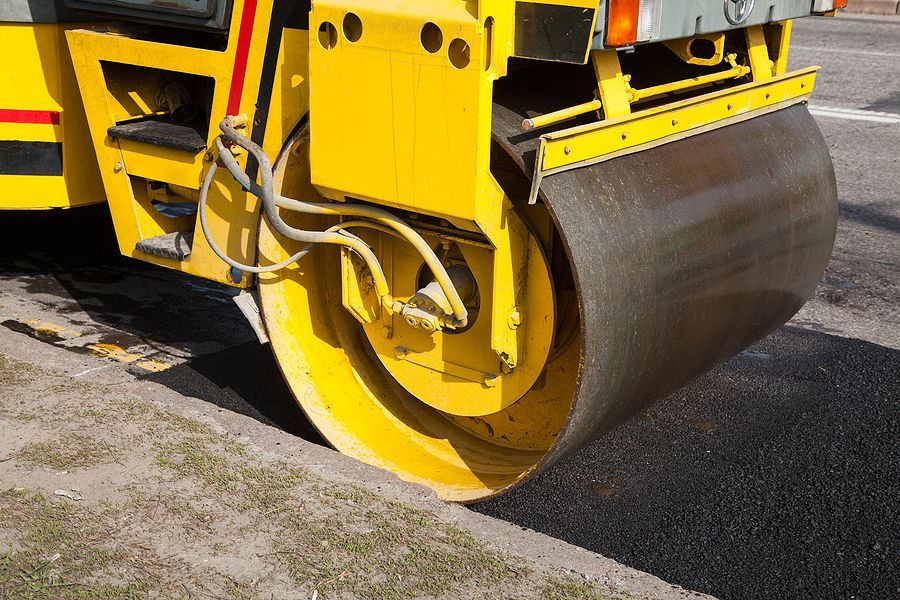 Yellow steamroller compacting fresh asphalt on a road.